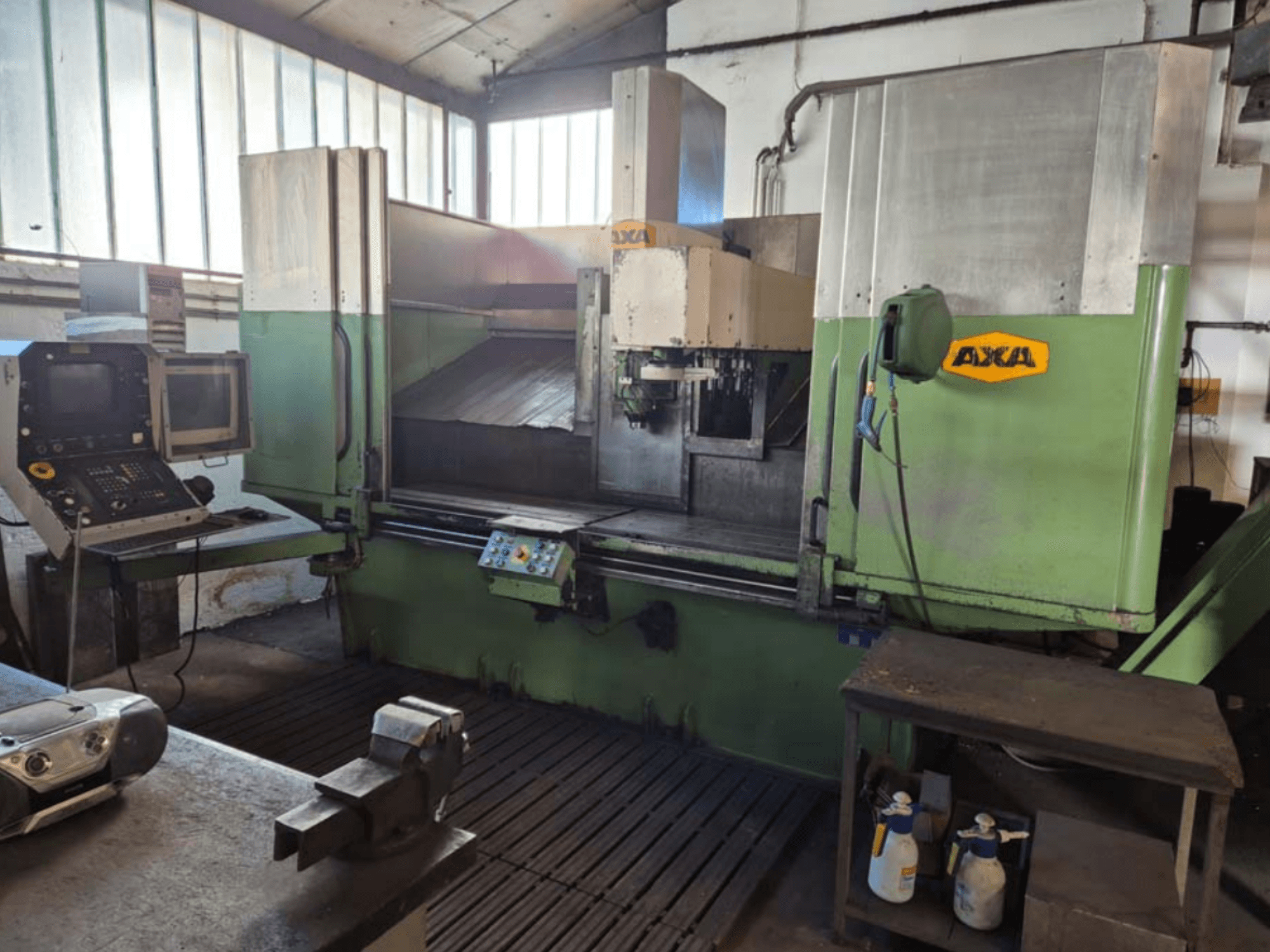 Centro di lavoro verticale AXA VSC-2M, vista frontale, con pannello di controllo e area di lavoro con utensili da taglio e materiale di pulizia.