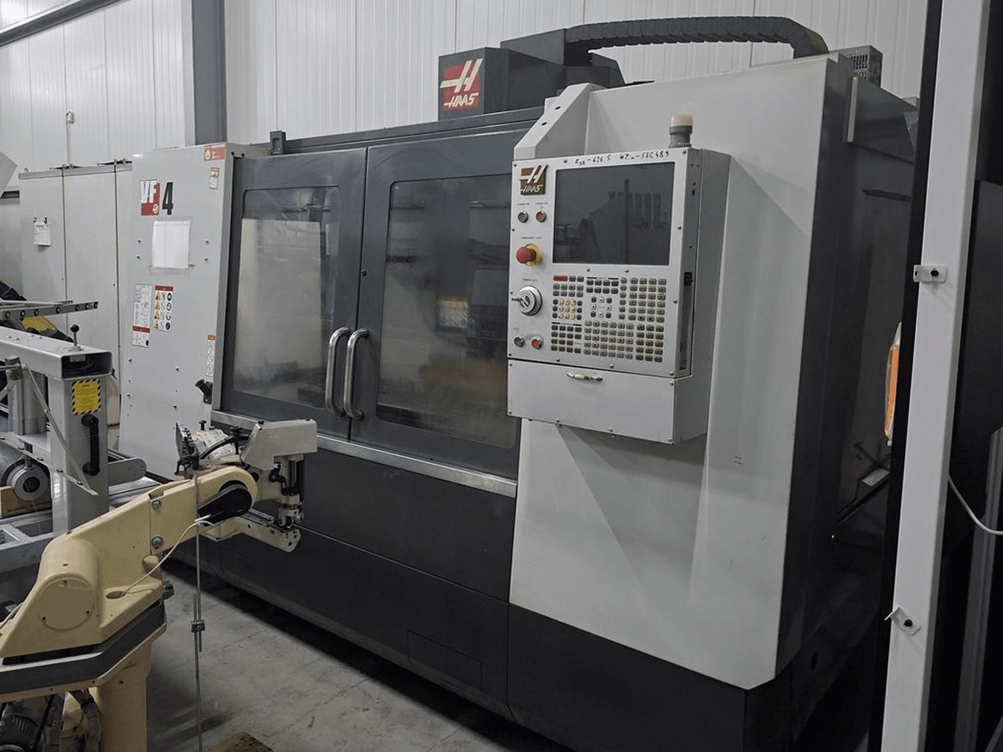 Fresatrice CNC Haas VF-4 in vista frontale, con pannello di controllo numerico e braccio robotico per l'automazione.