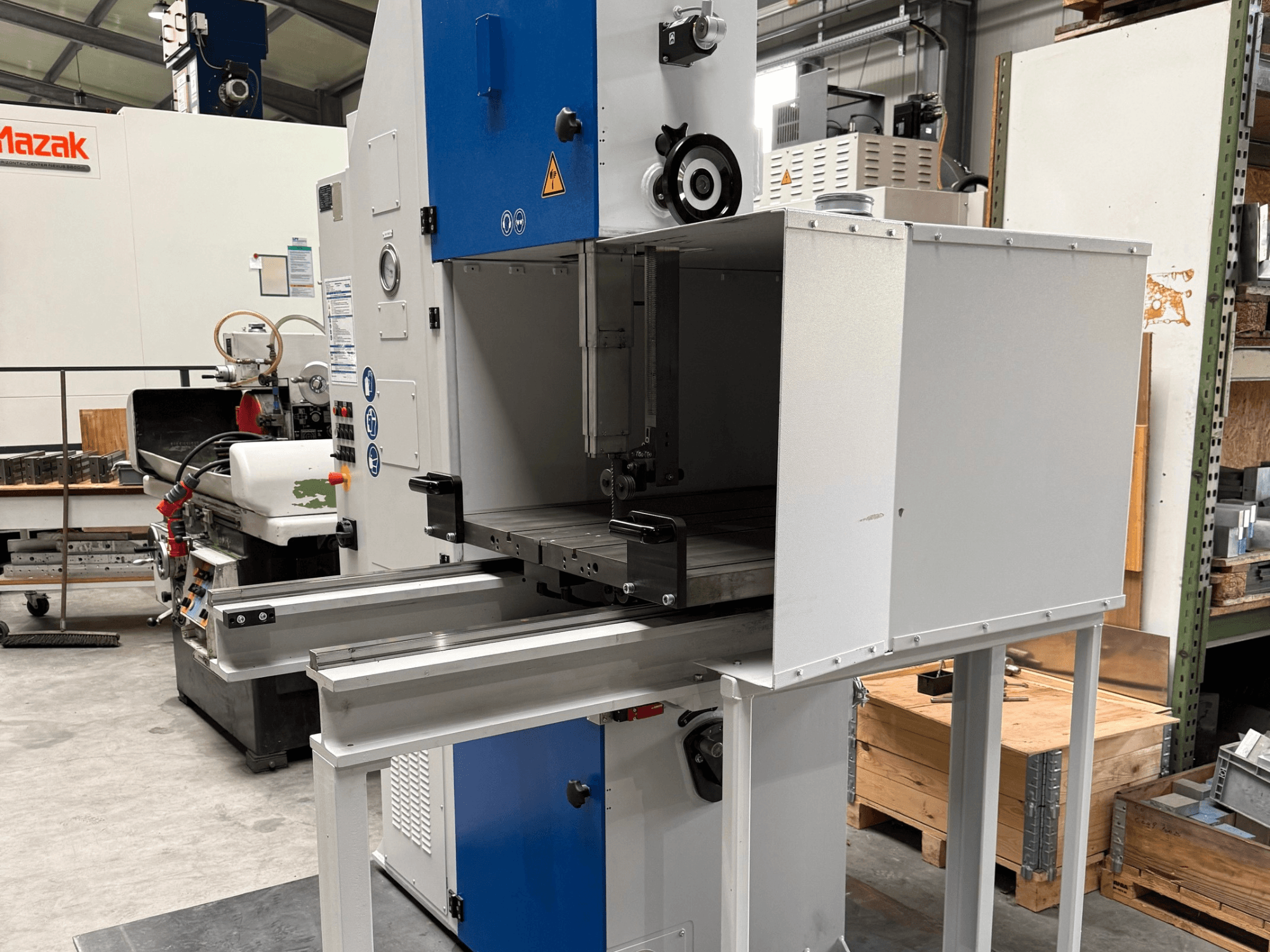 Macchina industriale Mazak vista frontalmente, con pannello di controllo blu, tavolo in metallo e avvisi di sicurezza.