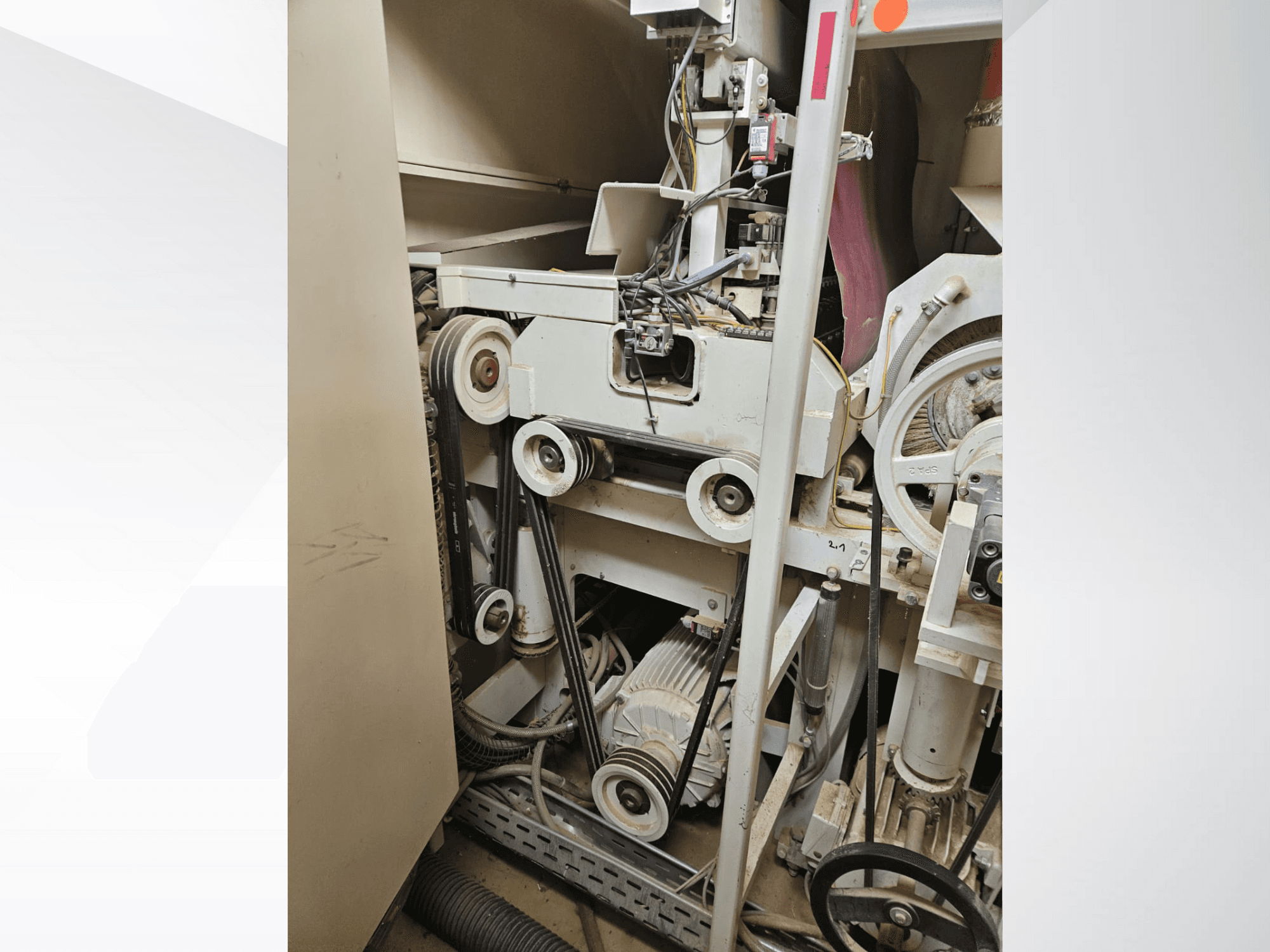 Interno di macchina industriale con cinghie e pulegge, con motore e cablaggio, visto di lato.