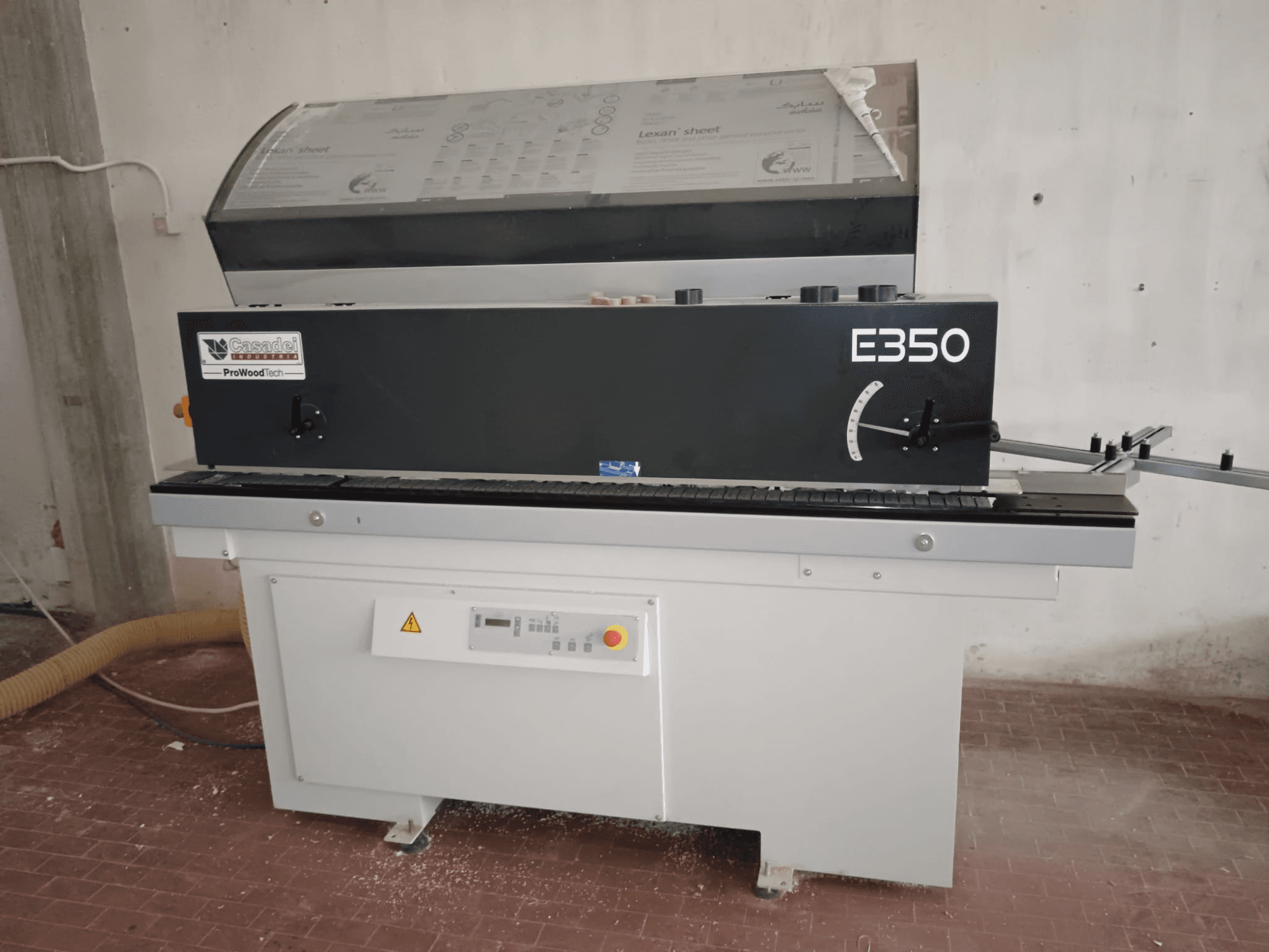 Cesaroli ProWoodtech E350, vista laterale di una macchina per la lavorazione del legno con pannello di controllo e accumulo di polvere, montata su una base bianca.