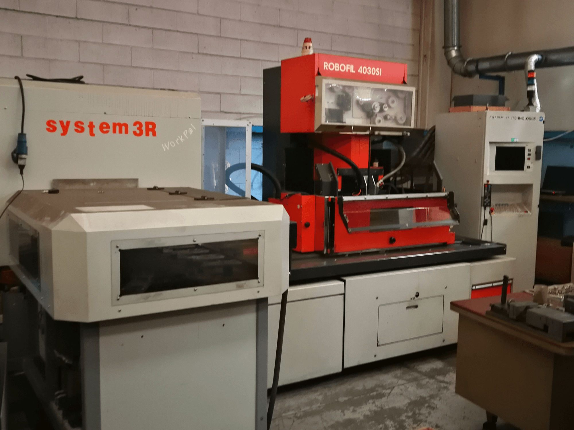 Vista frontale della macchina per elettroerosione a filo CHARMILLES ROBOFIL 4030 Si, caratterizzata da un esterno rosso e grigio e dalla stazione di lavoro system3R adiacente.