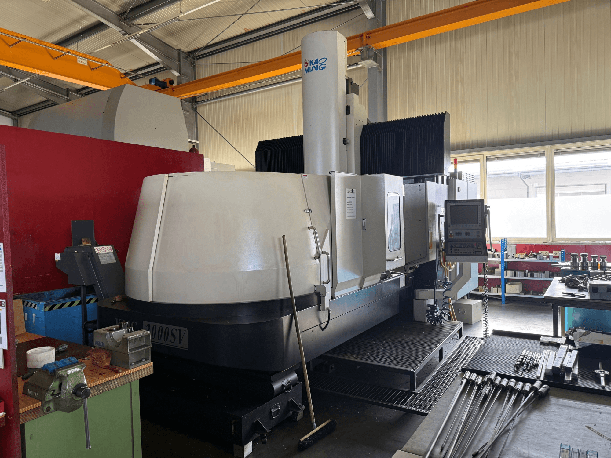 Fresatrice a portale KAOMING KMC-2000 SV in un'officina, vista frontale con pannello di controllo e utensili circostanti visibili.
