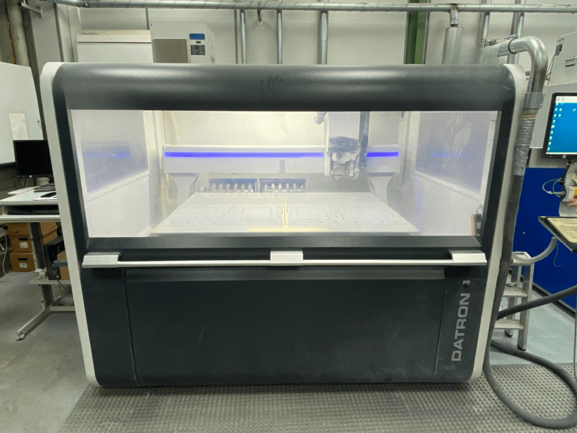 Vista frontale del Centro di lavoro verticale MLCube B di Datron, che mostra l'involucro trasparente e il pannello di controllo.