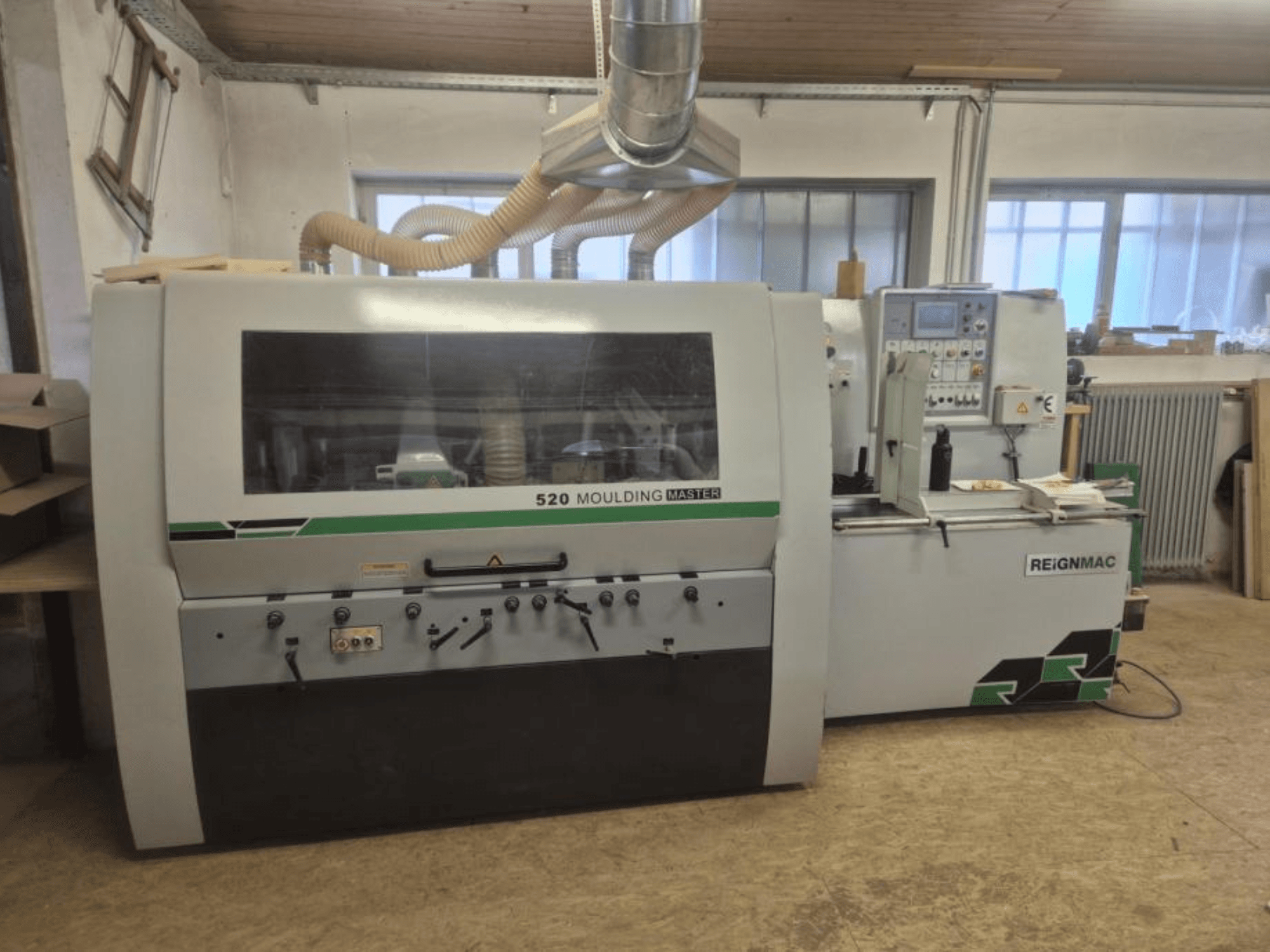 Vista frontale della pialla per legno REIGNMAC 520 MOULDING MASTER, che mostra il pannello di controllo, i rulli di alimentazione e il sistema di aspirazione della polvere.