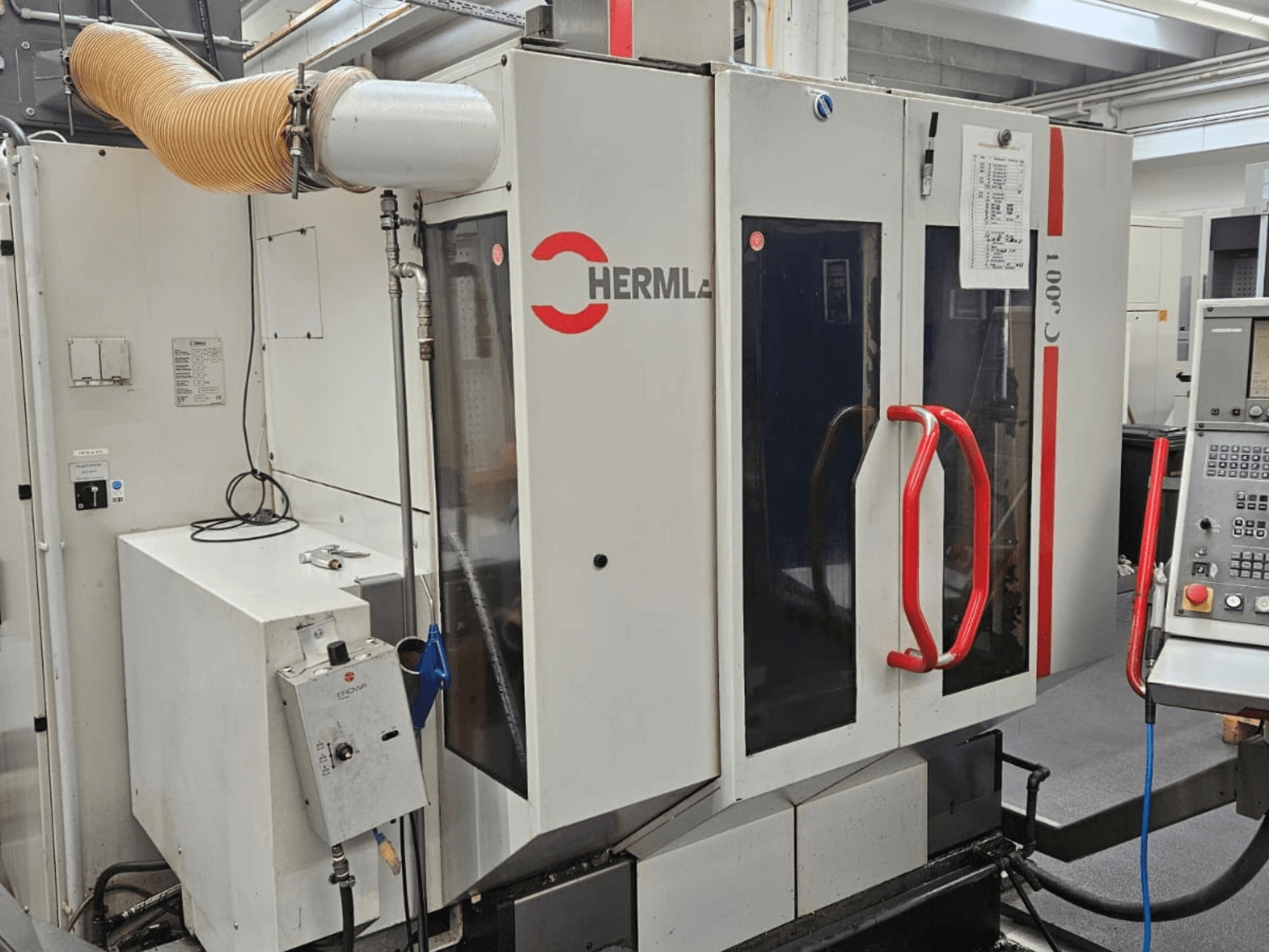 Vista frontale del centro di lavoro universale HERMLE C 600 U, che mostra il pannello di controllo e le maniglie rosse sulle porte.