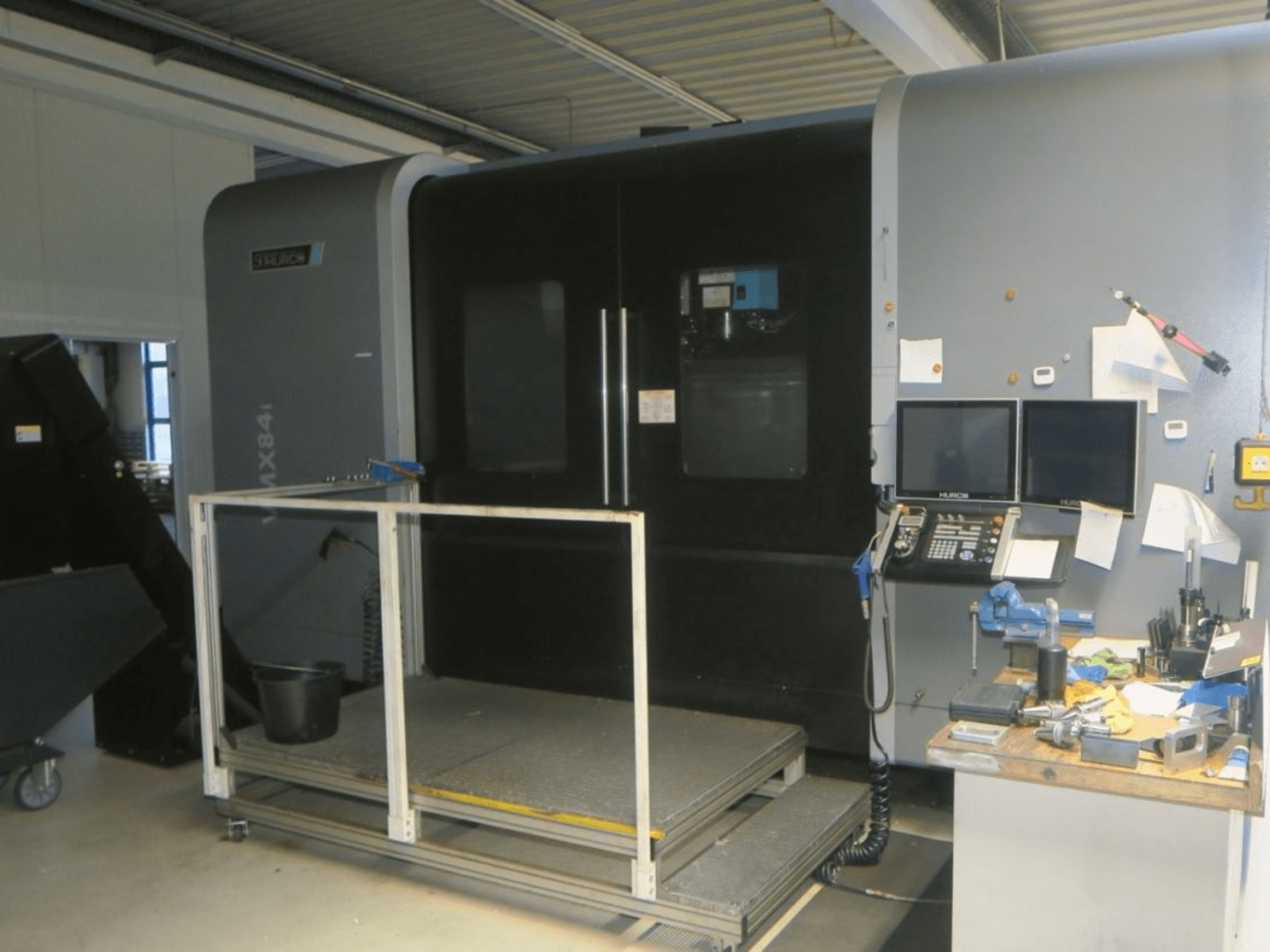 Macchina CNC Hurco MX84 in vista frontale, con doppio monitor, pannello di controllo e area di lavoro con vari utensili.