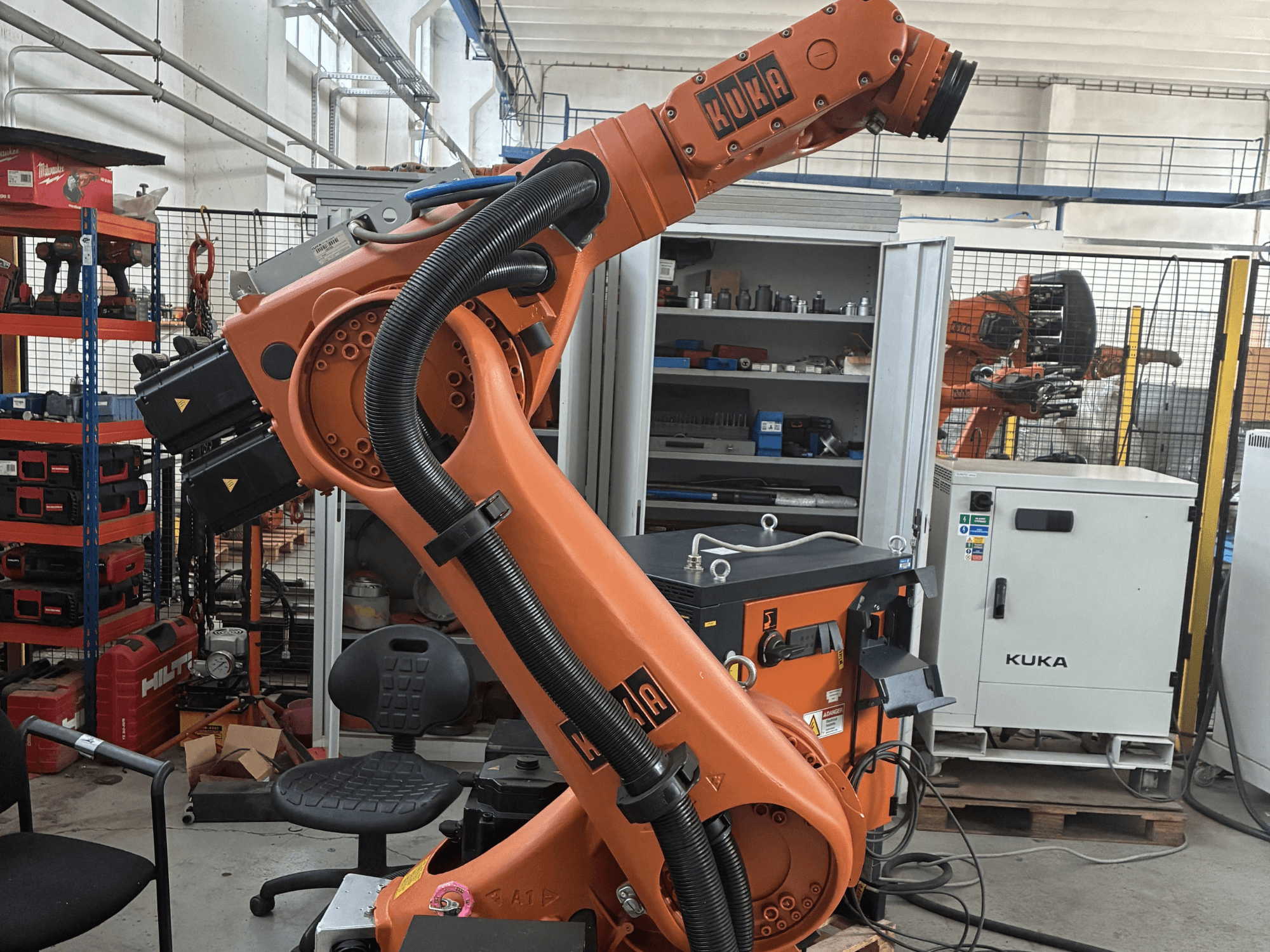 Braccio robotico KUKA KR30-3 in un ambiente industriale, vista laterale che mostra cavi e comandi, con strumenti e scaffali sullo sfondo.