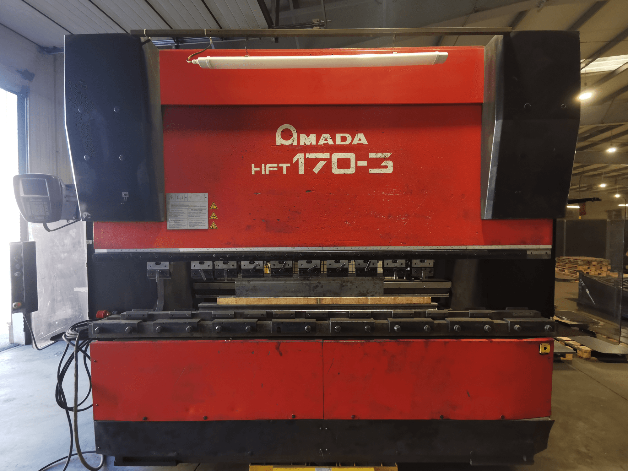 Pressa piegatrice Amada HFT 170-3 rossa vista frontalmente, con pannello di controllo, utensili di piegatura e piano di lavoro.