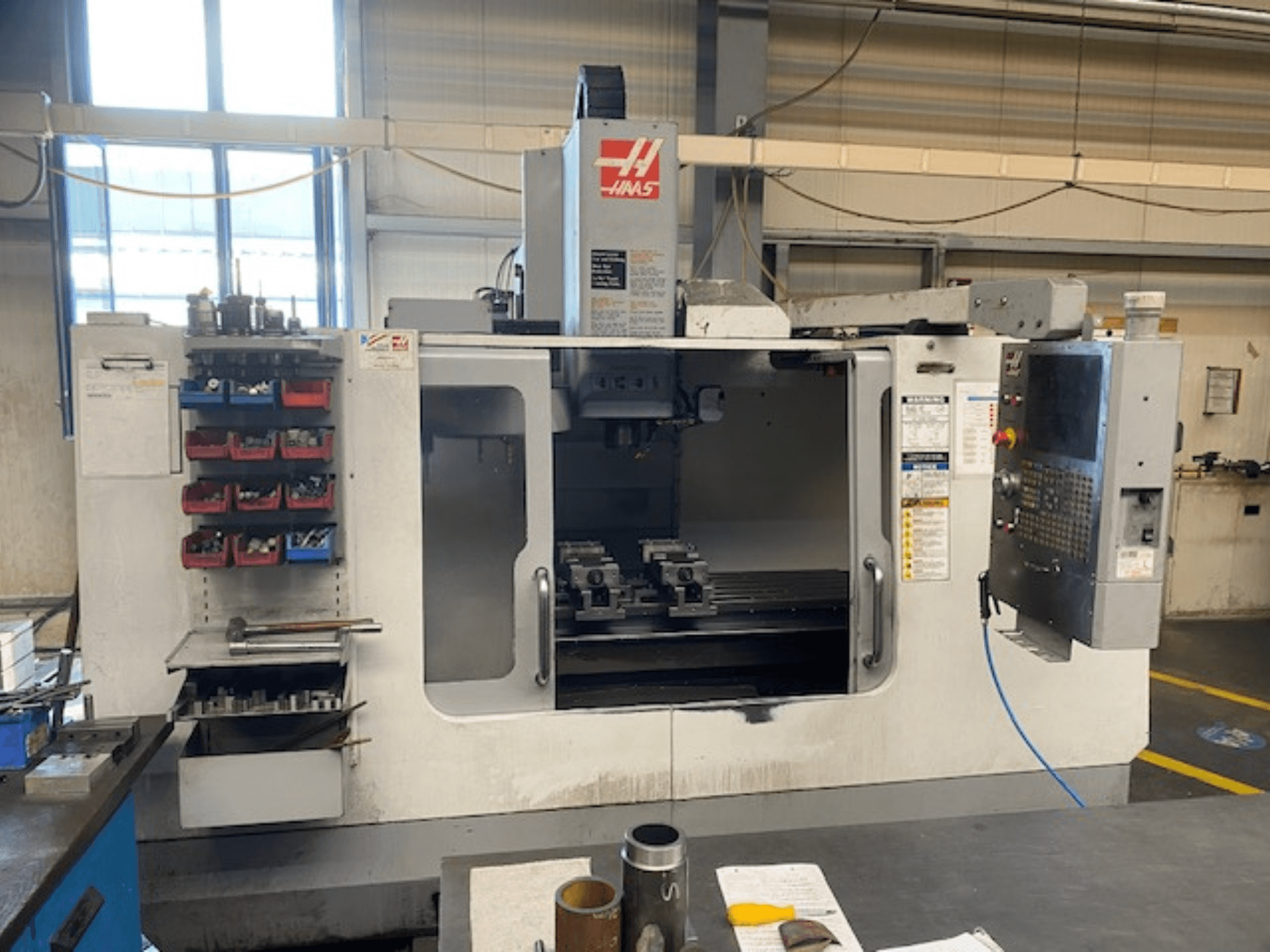 Vista frontale della fresatrice CNC Haas, modello VF-2, con magazzino utensili, pannello di controllo e strumenti dell'area di lavoro visibili.