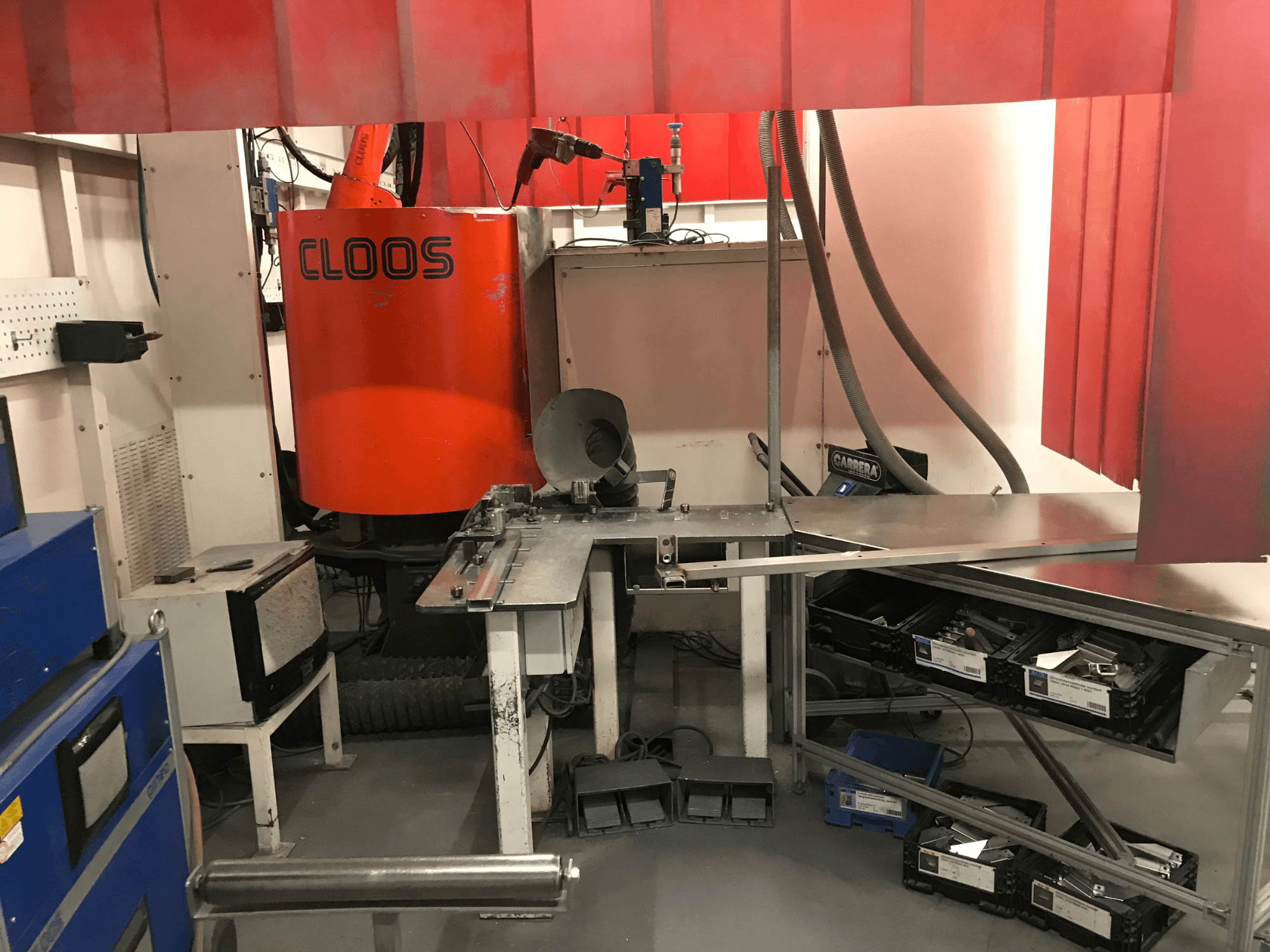 Sistema per officina di saldatura di DESSAUER, vista frontale che mostra il braccio robotico, il piano di lavoro in metallo e le aree di stoccaggio in un ambiente di officina.