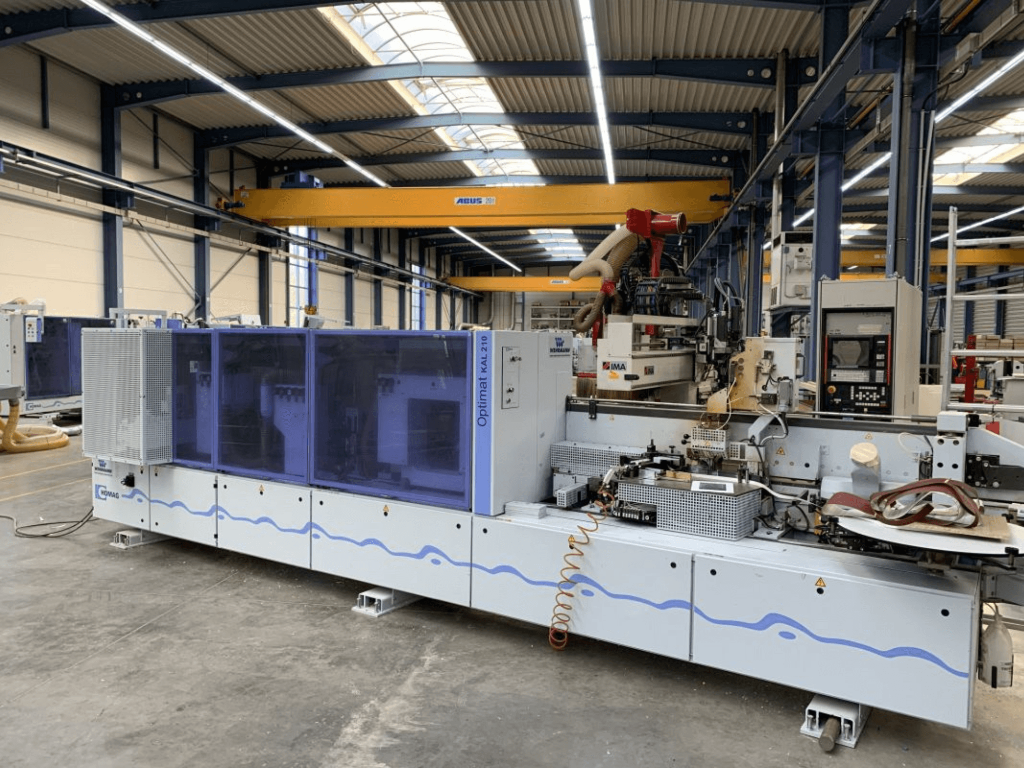 Bordatrice HOMAG Optimat KAL210 vista frontale, che mostra il pannello di controllo e l'area di lavorazione in un ambiente industriale.