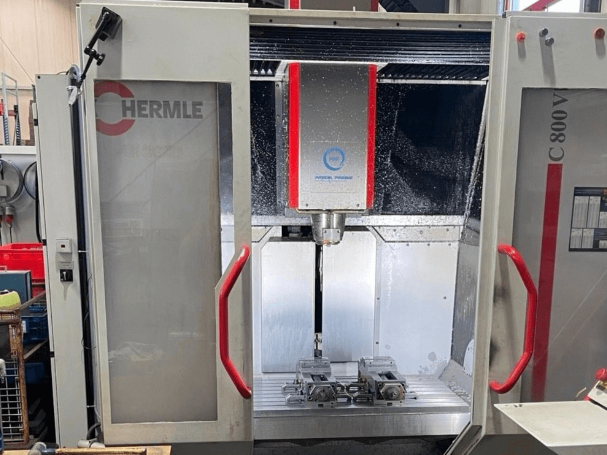 Centro di lavorazione verticale HERMLE C800V, vista frontale che mostra l’area di lavorazione con i pezzi e il liquido di raffreddamento.
