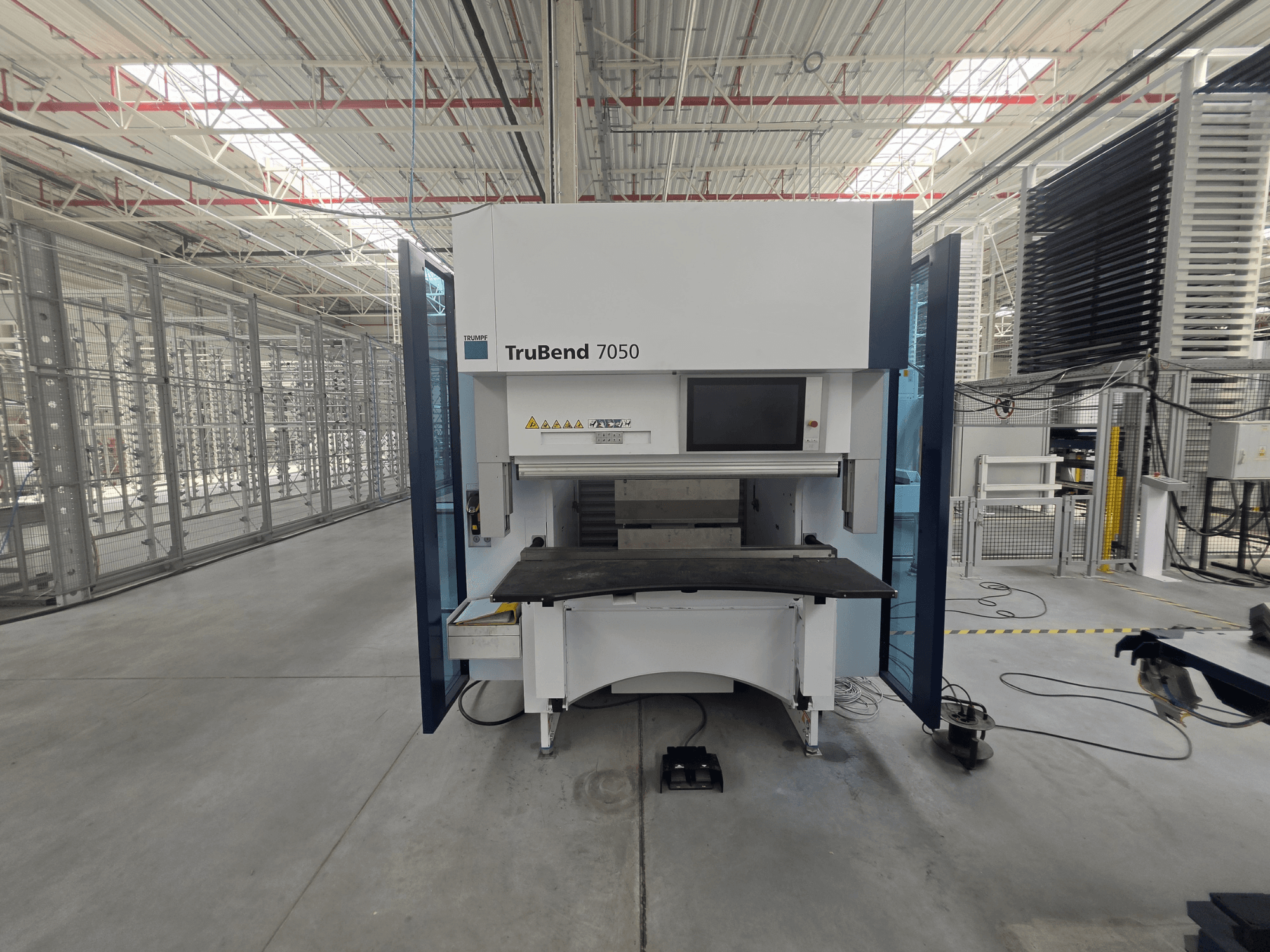 Vista frontale della pressa piegatrice TRUMPF TruBend 7050, con il pannello di controllo e il piano di lavoro in primo piano in un ambiente industriale ben illuminato.