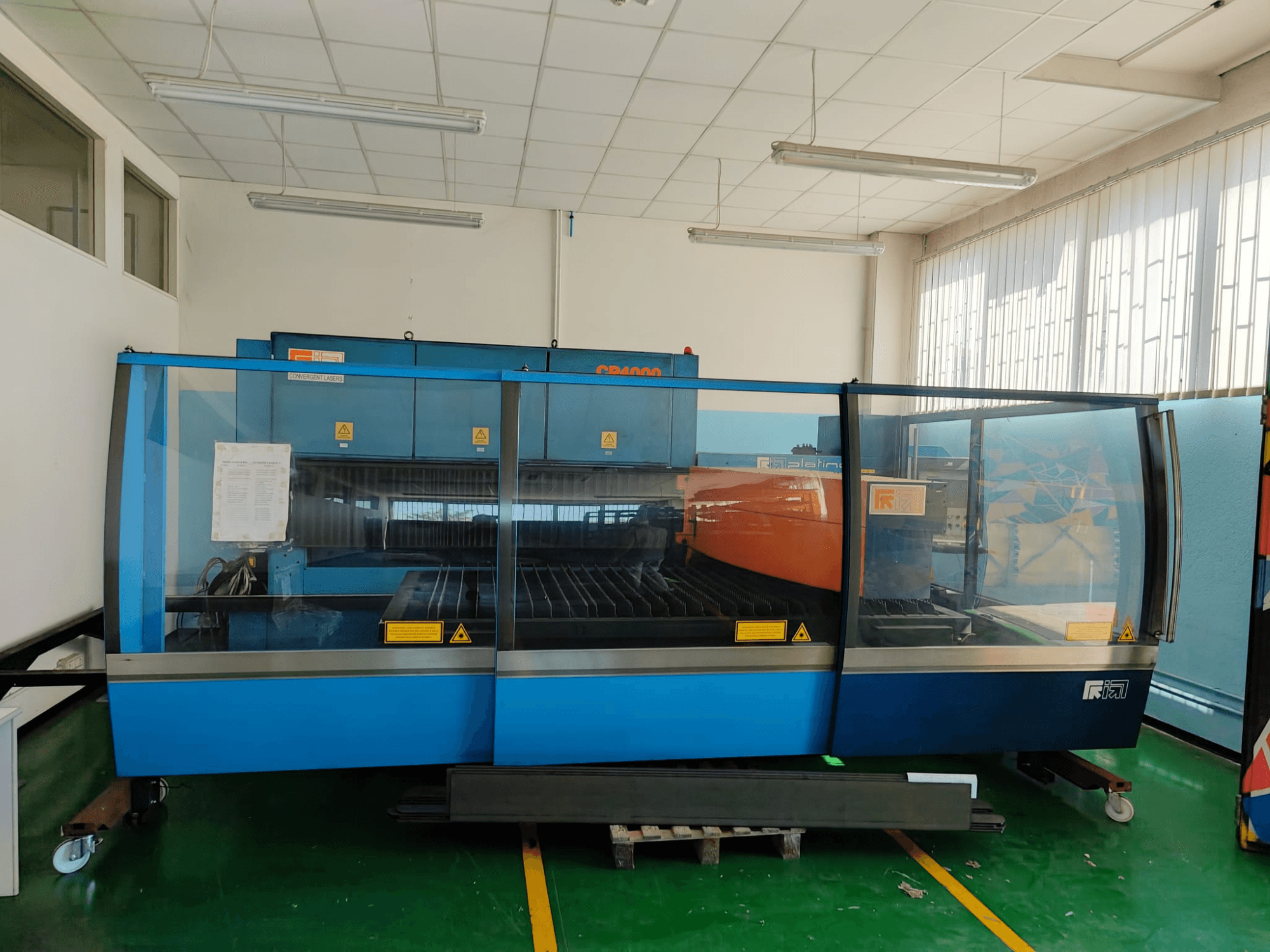 Vista frontale di una macchina per il taglio laser a CO₂ CP4000 di CONVERGENT LASERS, caratterizzata da un design nei colori blu e arancione, all’interno di un’officina ben illuminata.