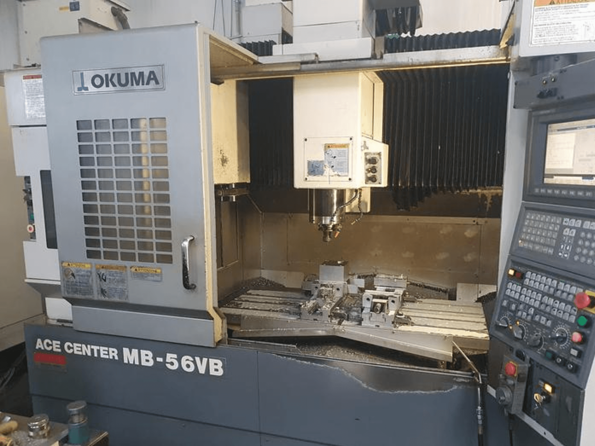 La fresatrice CNC Okuma ACE CENTER MB-56VB in una vista frontale, che mostra il pannello di controllo e l'area di lavorazione.
