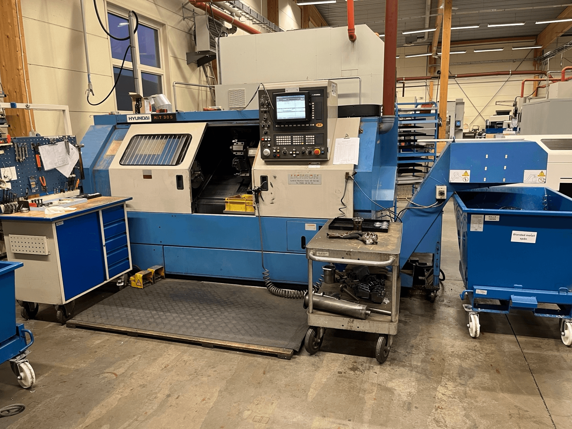 Tornio orizzontale Hyundai HIT 30S, vista frontale, con pannello di controllo e utensili su un carrello vicino in un'officina.