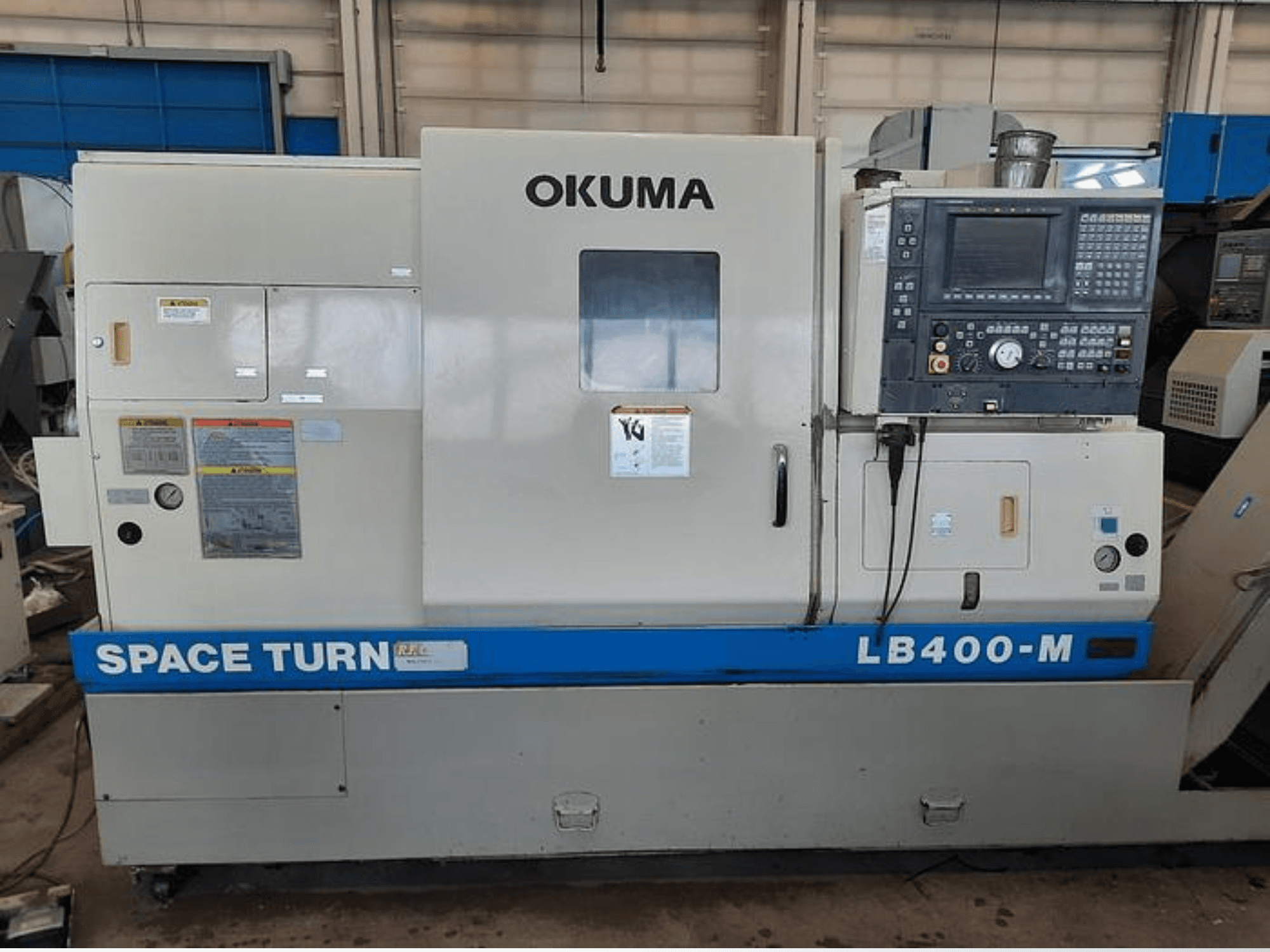 Tornio CNC Okuma LB400-M, vista frontale con pannello di controllo, etichette di avvertenza e marchio blu "SPACE TURN" visibile.