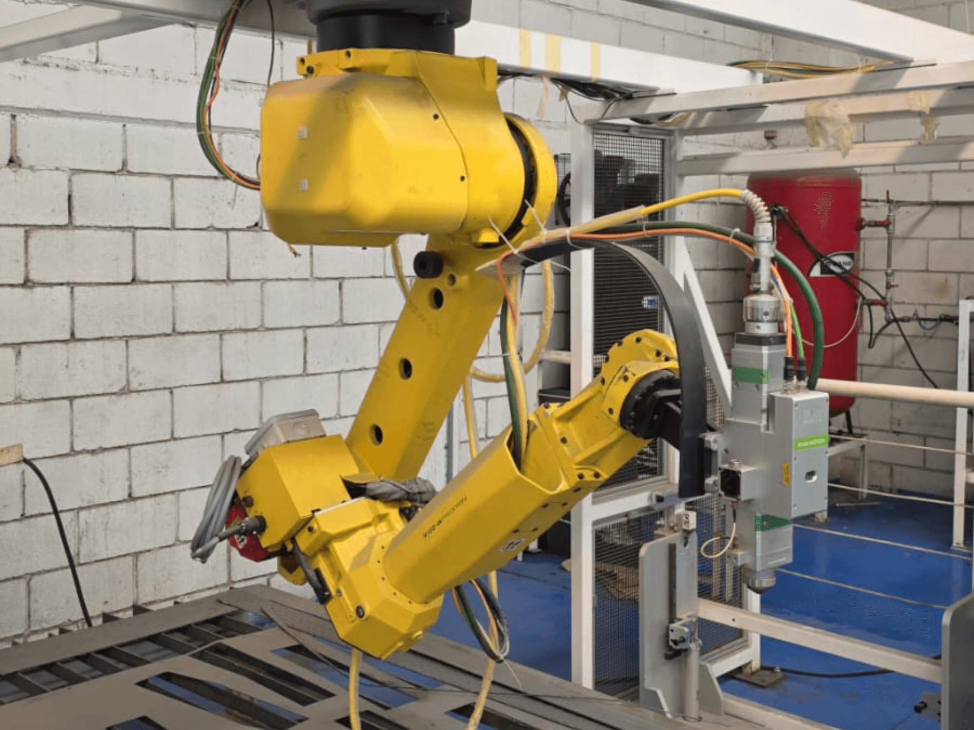 Braccio robotico giallo con un utensile di precisione, dotato di più giunti e cavi, visto da un'angolazione frontale in un ambiente industriale.
