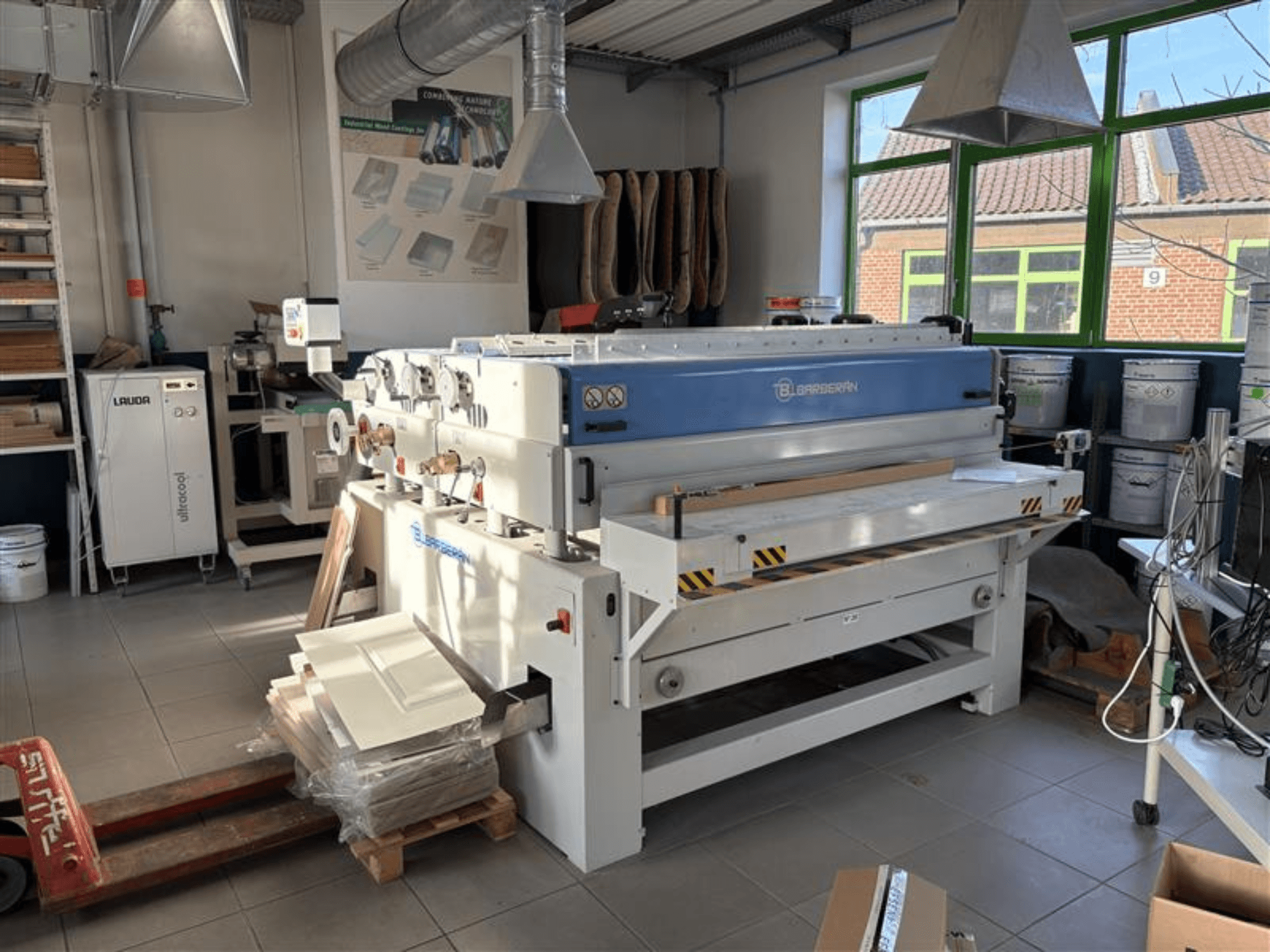 Macchina per la lavorazione del legno Blaserbn in un'officina, vista frontale; con pannelli di legno su un pallet e attrezzature moderne sullo sfondo.