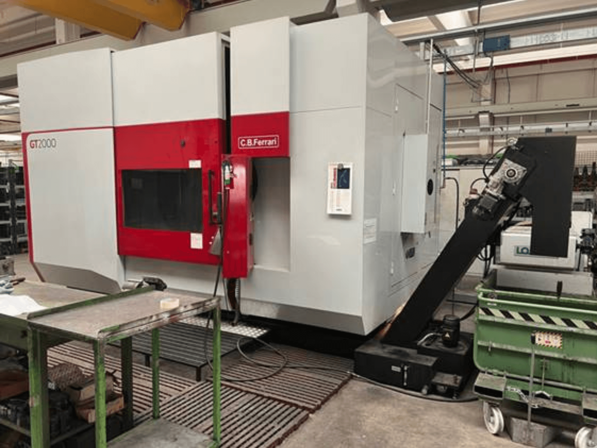 Fresatrice C.B. Ferrari GT2000 in vista frontale, con braccio robotico e area di lavoro industriale con carrello verde.