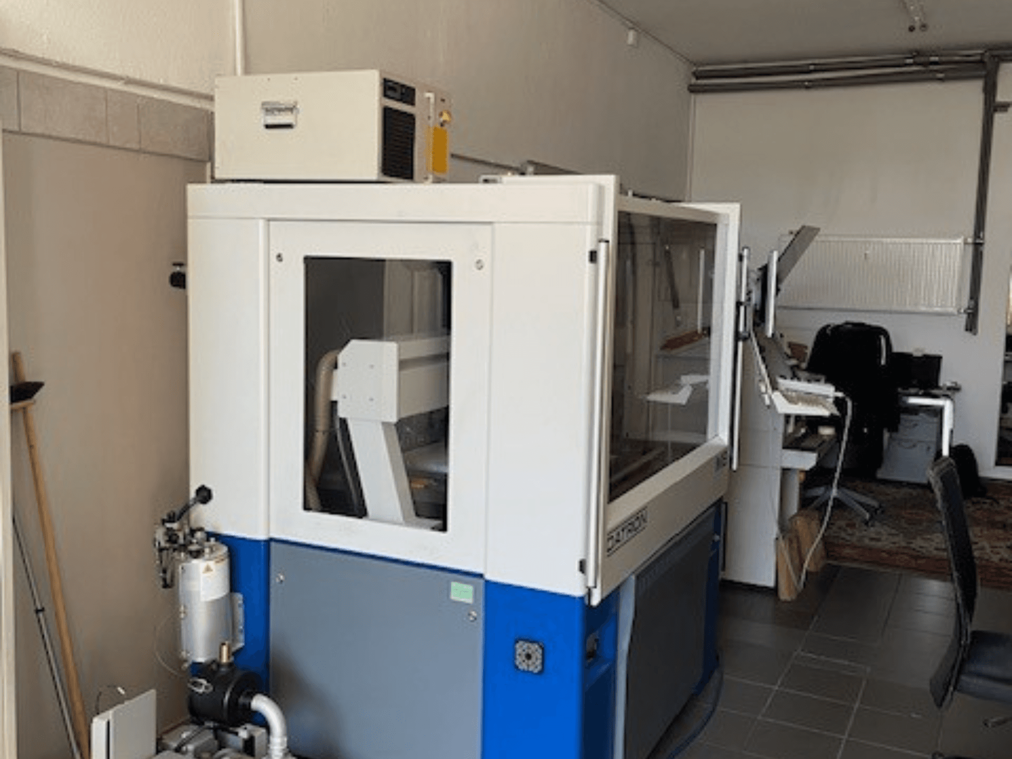 Macchina industriale blu e bianca con pannelli trasparenti, vista frontale, include accesso di controllo e unità di ventilazione visibile.