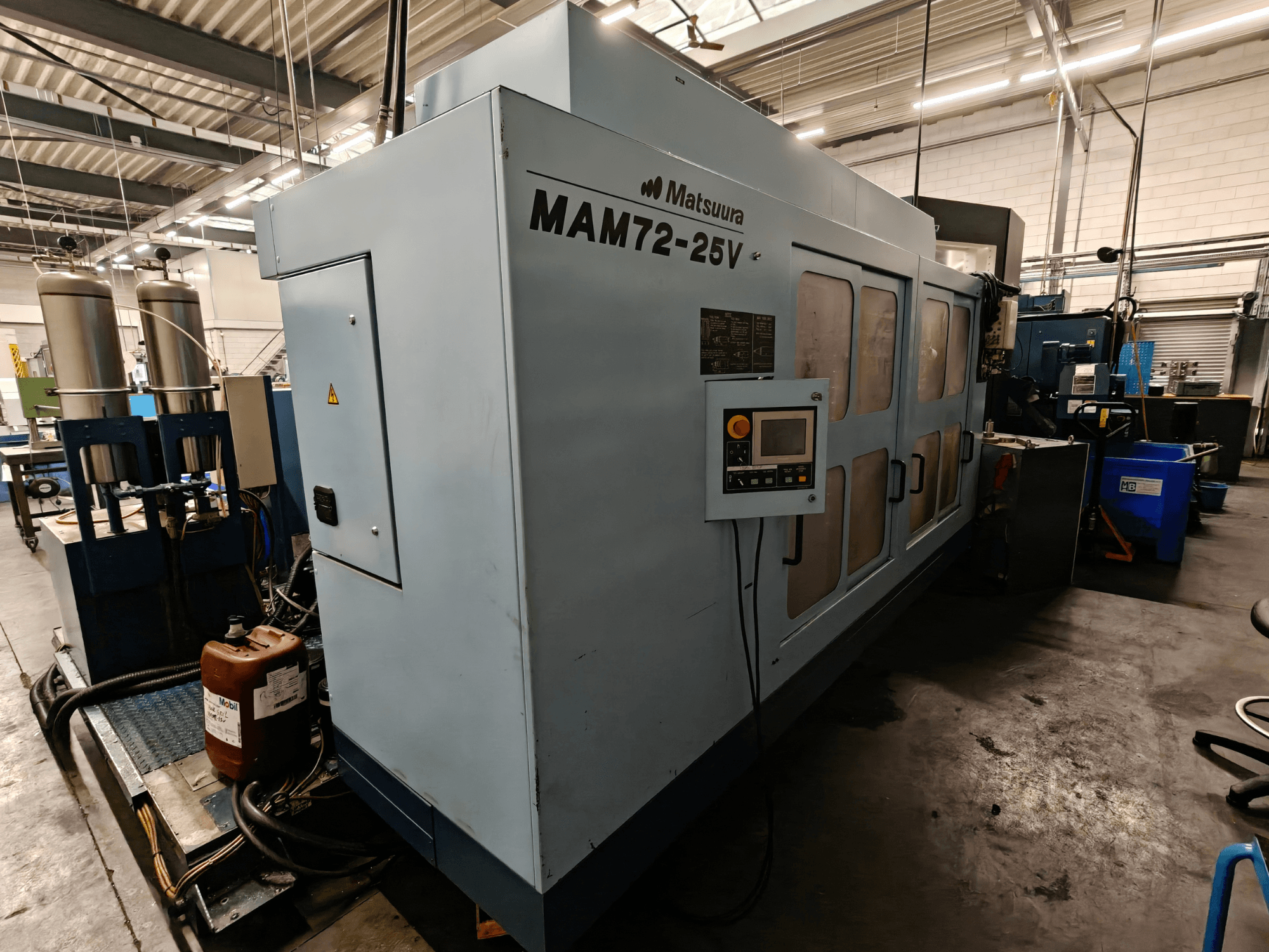 Macchina CNC Matsuura MAM72-25V, vista laterale, con pannello di controllo, doppio serbatoio del refrigerante e area di lavoro in un ambiente industriale.