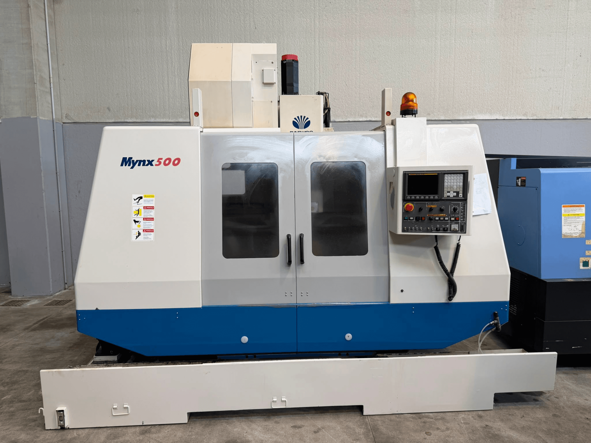 Centro di lavorazione verticale DAEWOO MYNX 500 visto frontalmente, con pannello di controllo, luci di sicurezza e sportelli di accesso trasparenti.