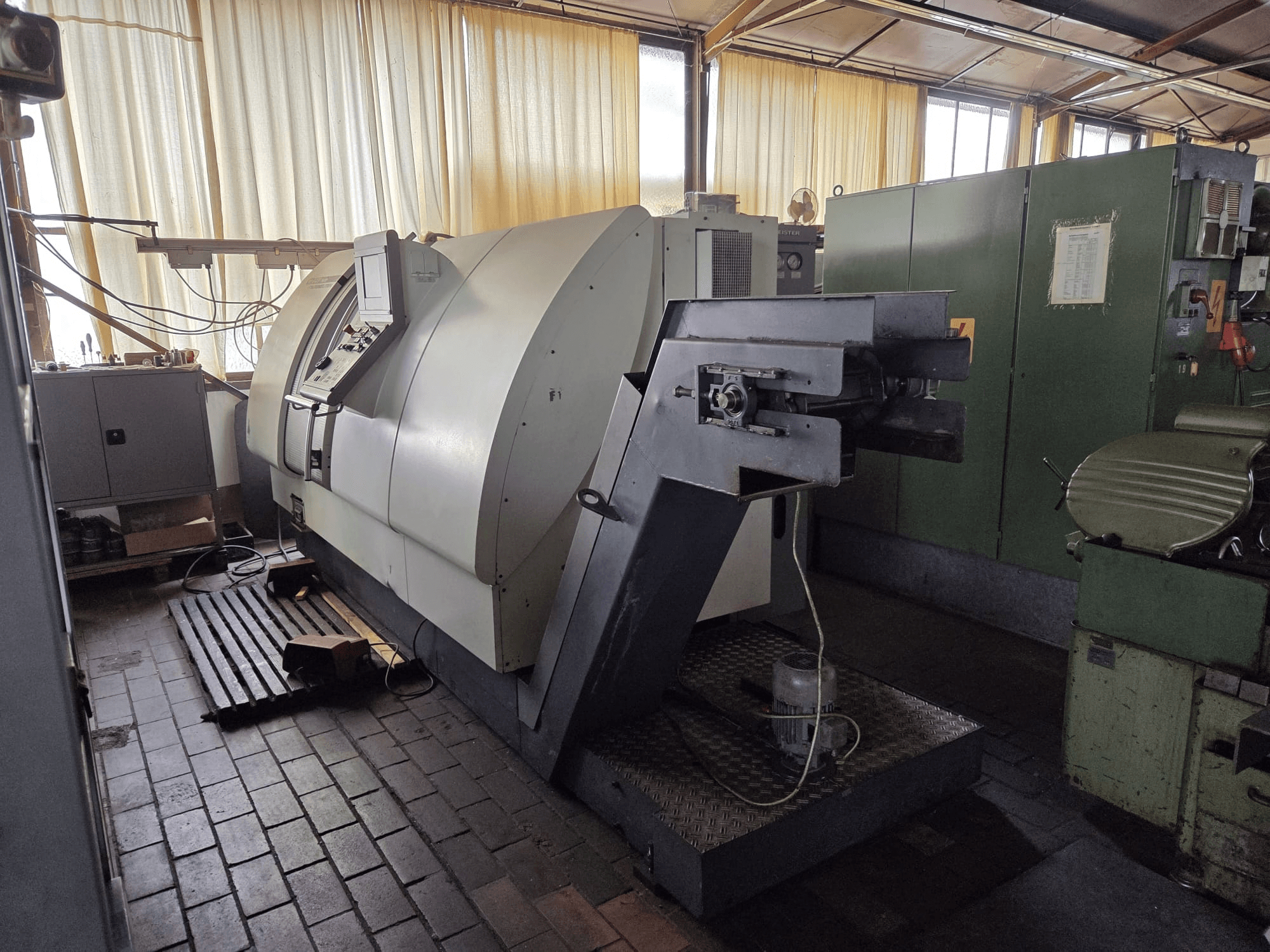 Centro di tornitura e fresatura Gildemeister CTX 400 a doppio mandrino, vista laterale, che mostra il pannello di controllo, l’ampio telaio e i macchinari adiacenti nell’officina.