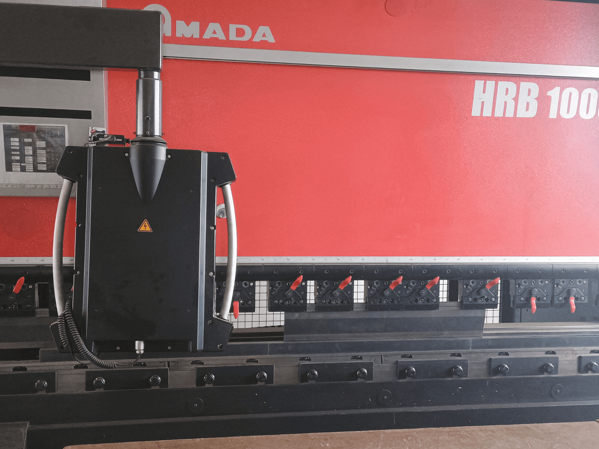 Vista frontale della piegatrice Amada HRB 100; presenta una testa di controllo nera con ugello conico e pinze regolabili.