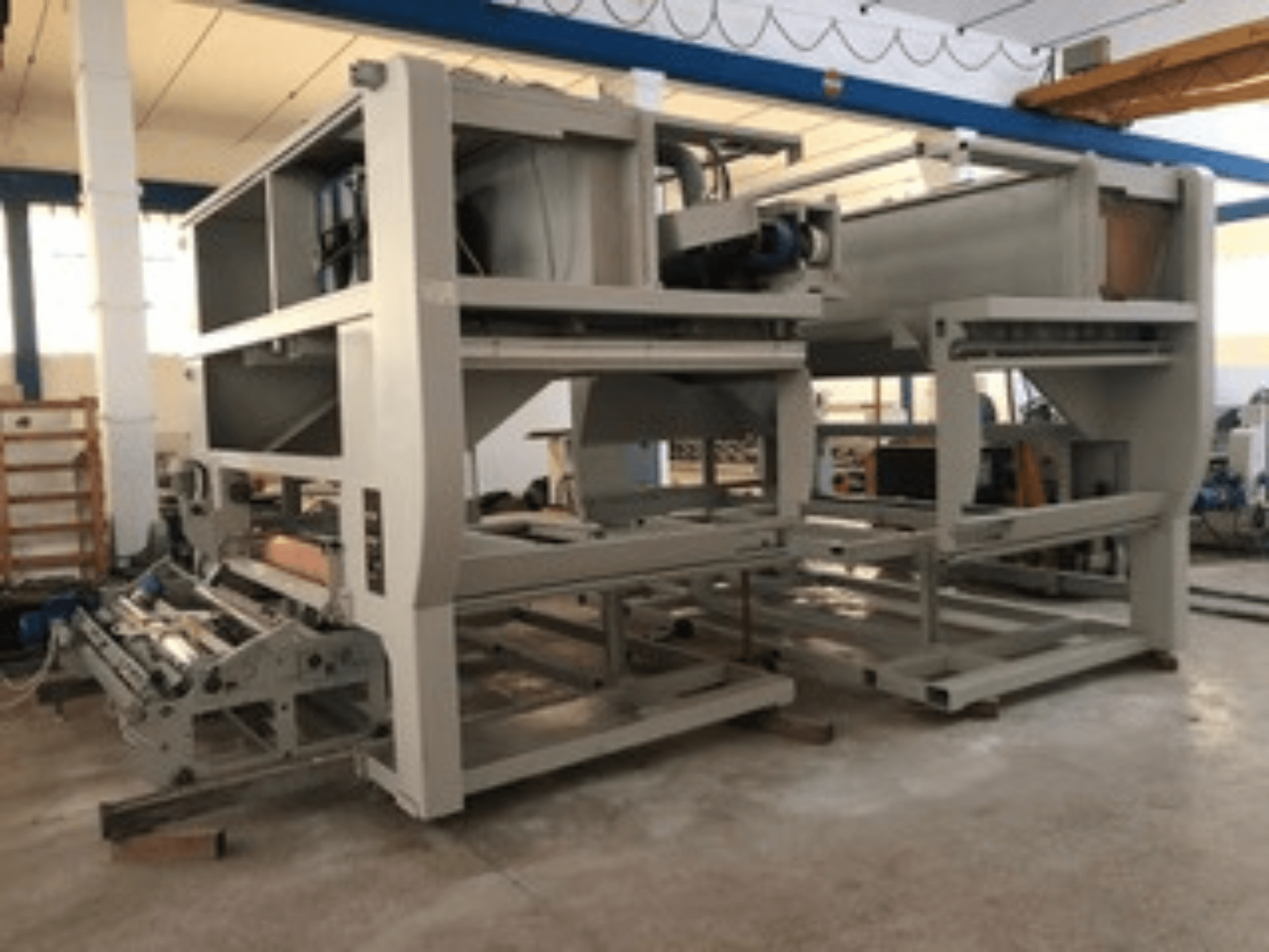 Macchina industriale con rulli trasportatori multipli e struttura di grandi dimensioni; vista laterale, colore grigio, situata in una fabbrica ben illuminata.