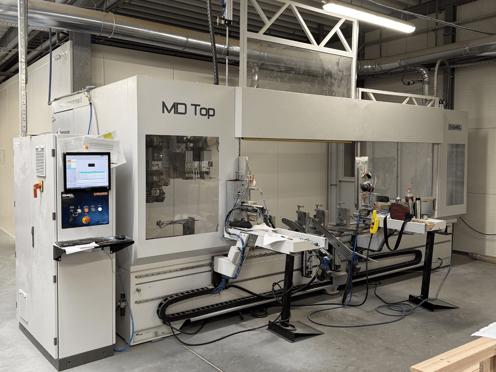 Macchina CNC MD Top vista frontalmente, con pannello di controllo, bracci robotici e area di lavoro con utensili e materiali.