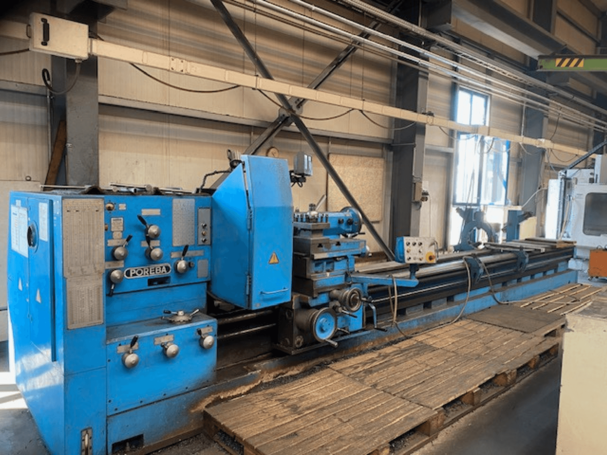 Vista frontale di un tornio POREBA blu, con manopole di controllo, poggiautensili e pallet di legno sottostanti.