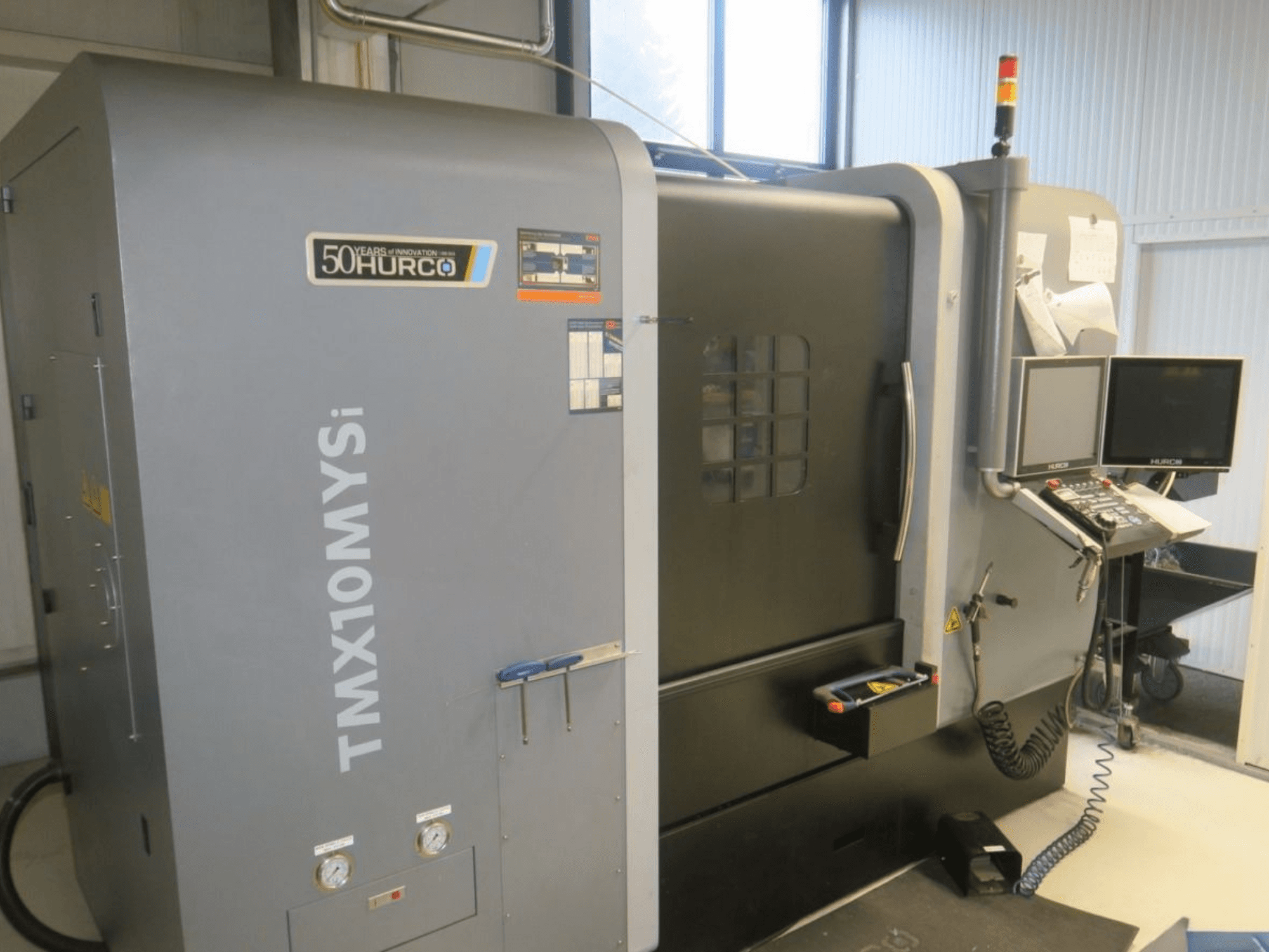 Macchina CNC Hurco TMX10MYSi in vista laterale; pannello di controllo, luci di emergenza e indicatori visualizzati.