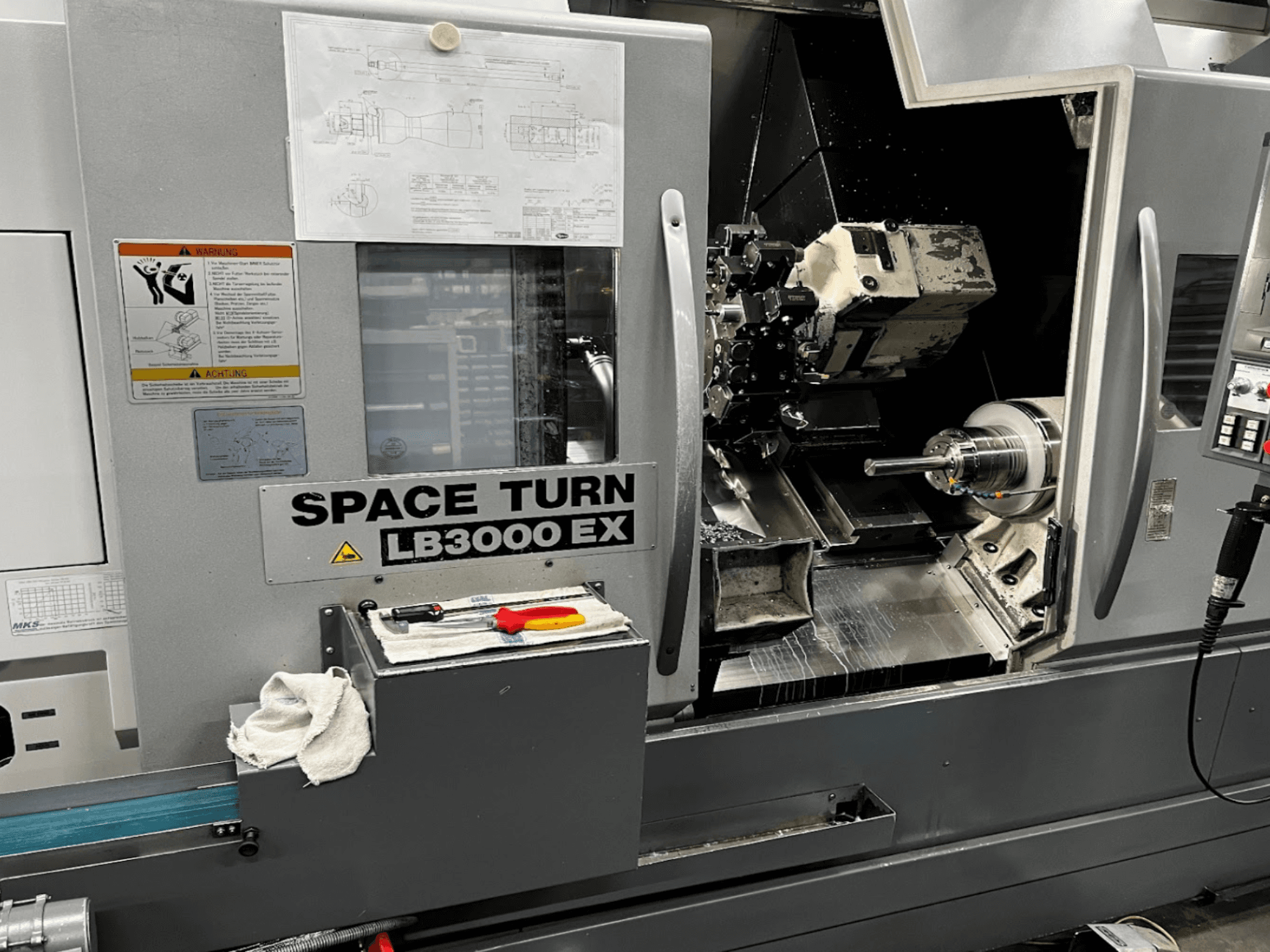 Tornio orizzontale Okuma LB3000EX MYW, vista frontale con pannello di controllo, utensili e dettagli dello spazio di lavoro visibili.