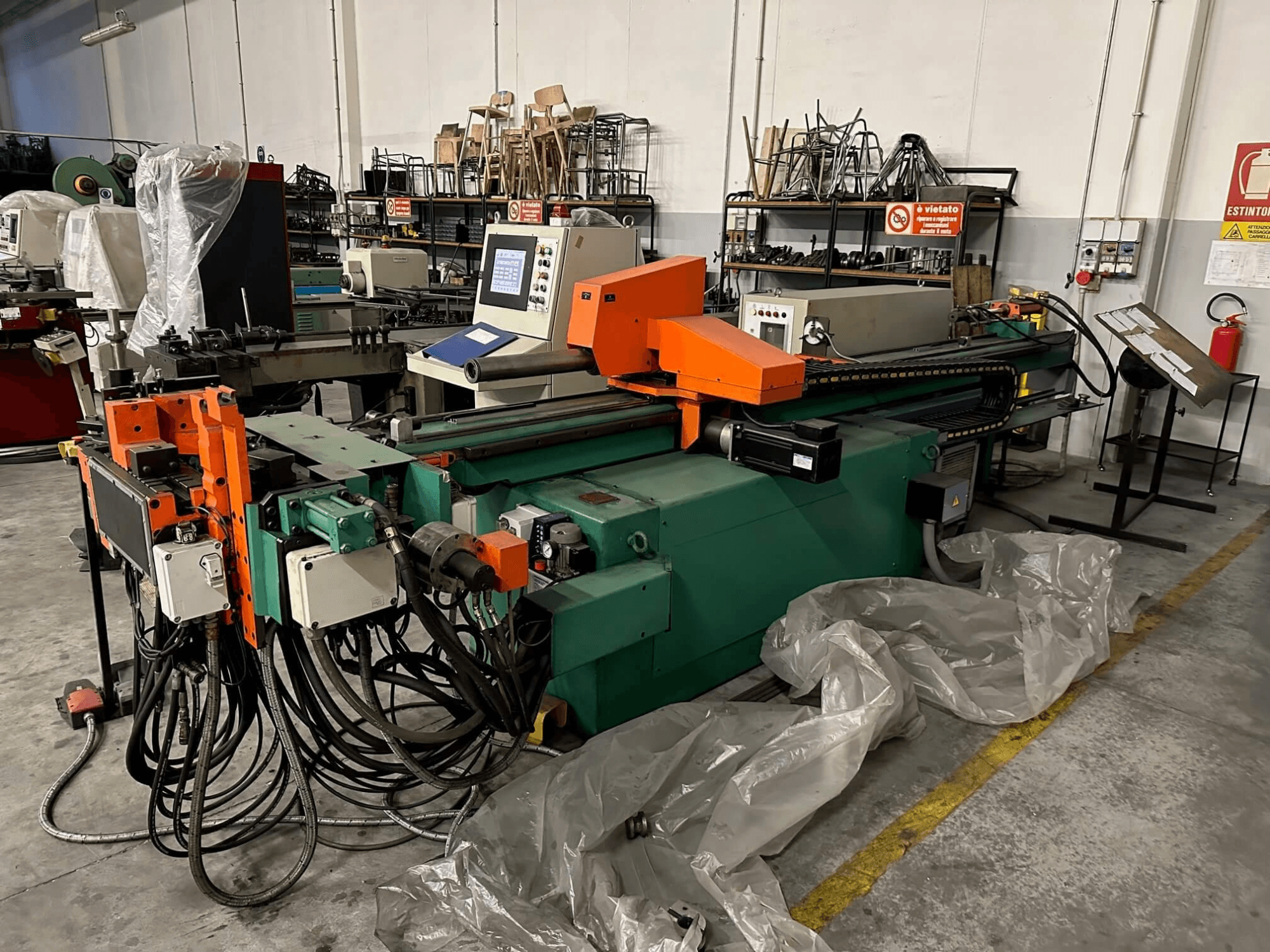 Macchina industriale con corpo arancione e verde, pannello di controllo e numerosi cavi, vista frontalmente in un'officina.