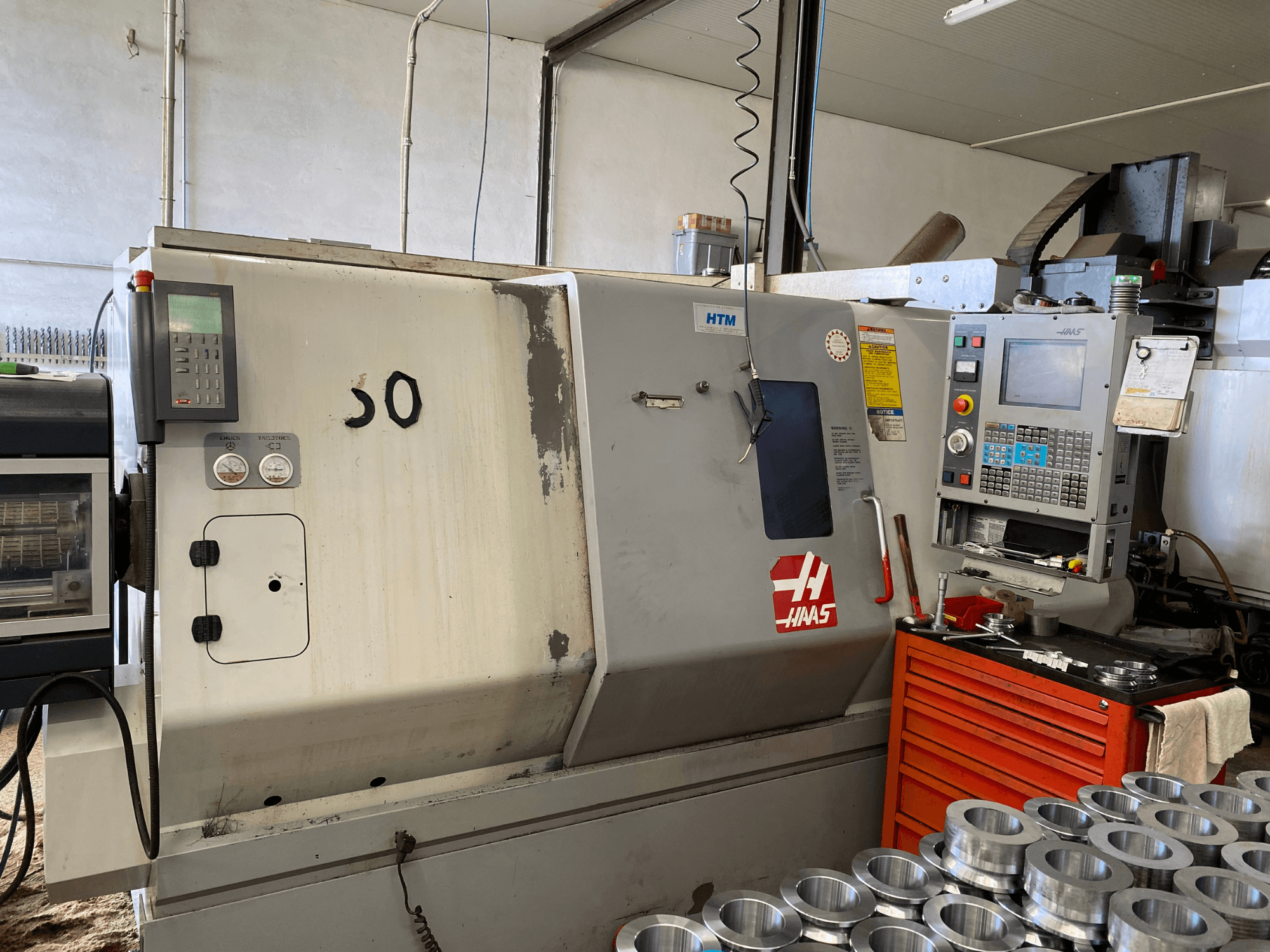 Macchina CNC Haas con pannello di controllo, vista frontale, che mostra i pulsanti operativi, gli indicatori e le parti metalliche impilate nelle vicinanze.