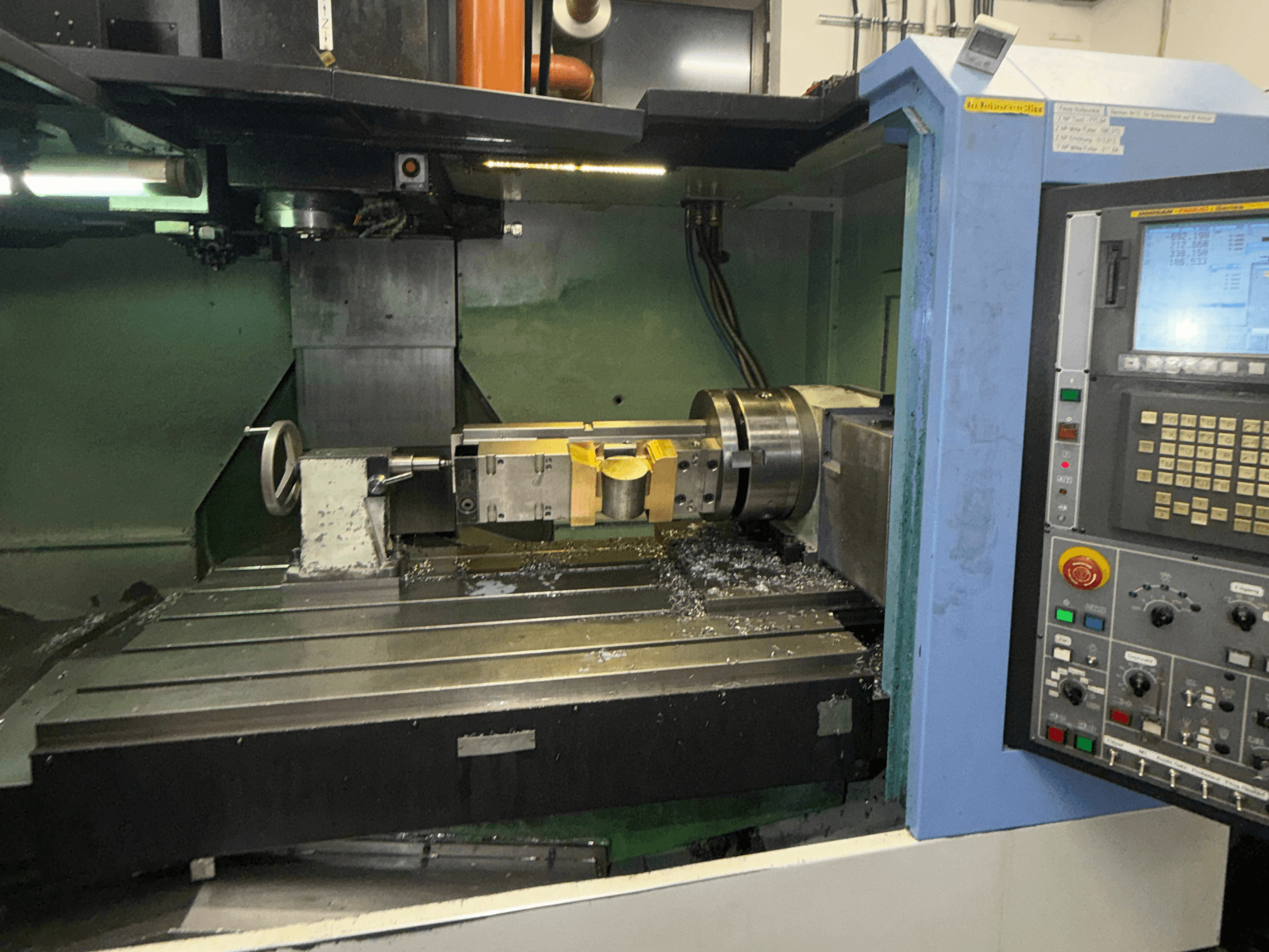 Centro di lavorazione verticale DOOSAN DNM650, vista frontale, che mostra l'utensile da taglio e il pannello di controllo, con trucioli metallici visibili sul piano di lavoro.