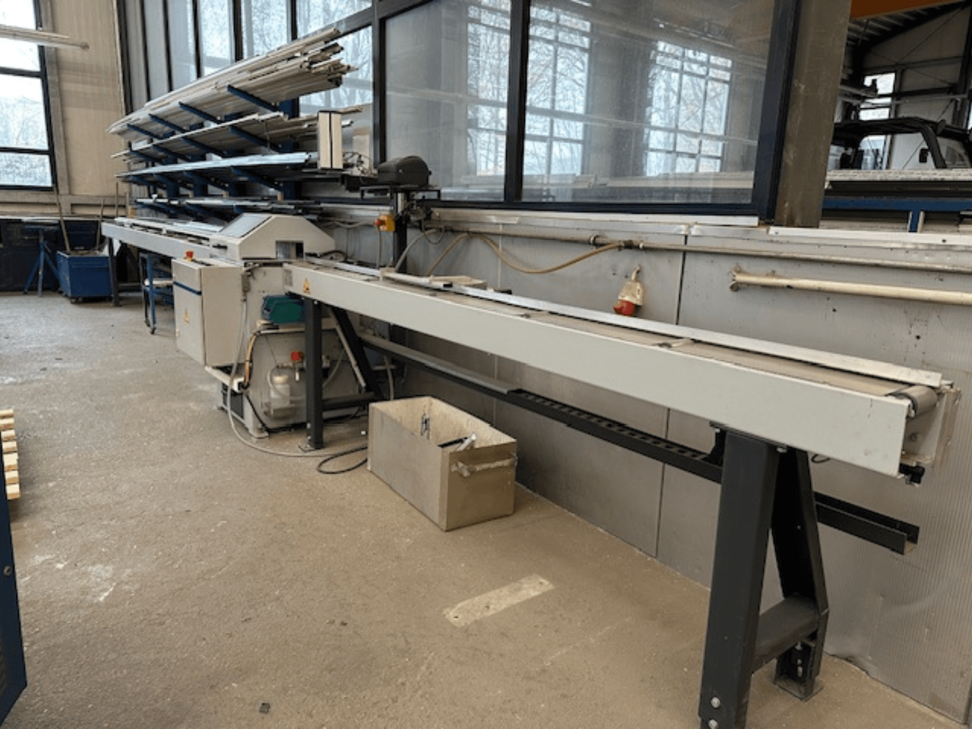 Sega circolare per metalli SCHÜCO PGS in un'officina, vista laterale con un piano di taglio regolabile e un ripiano di profili metallici sopra.