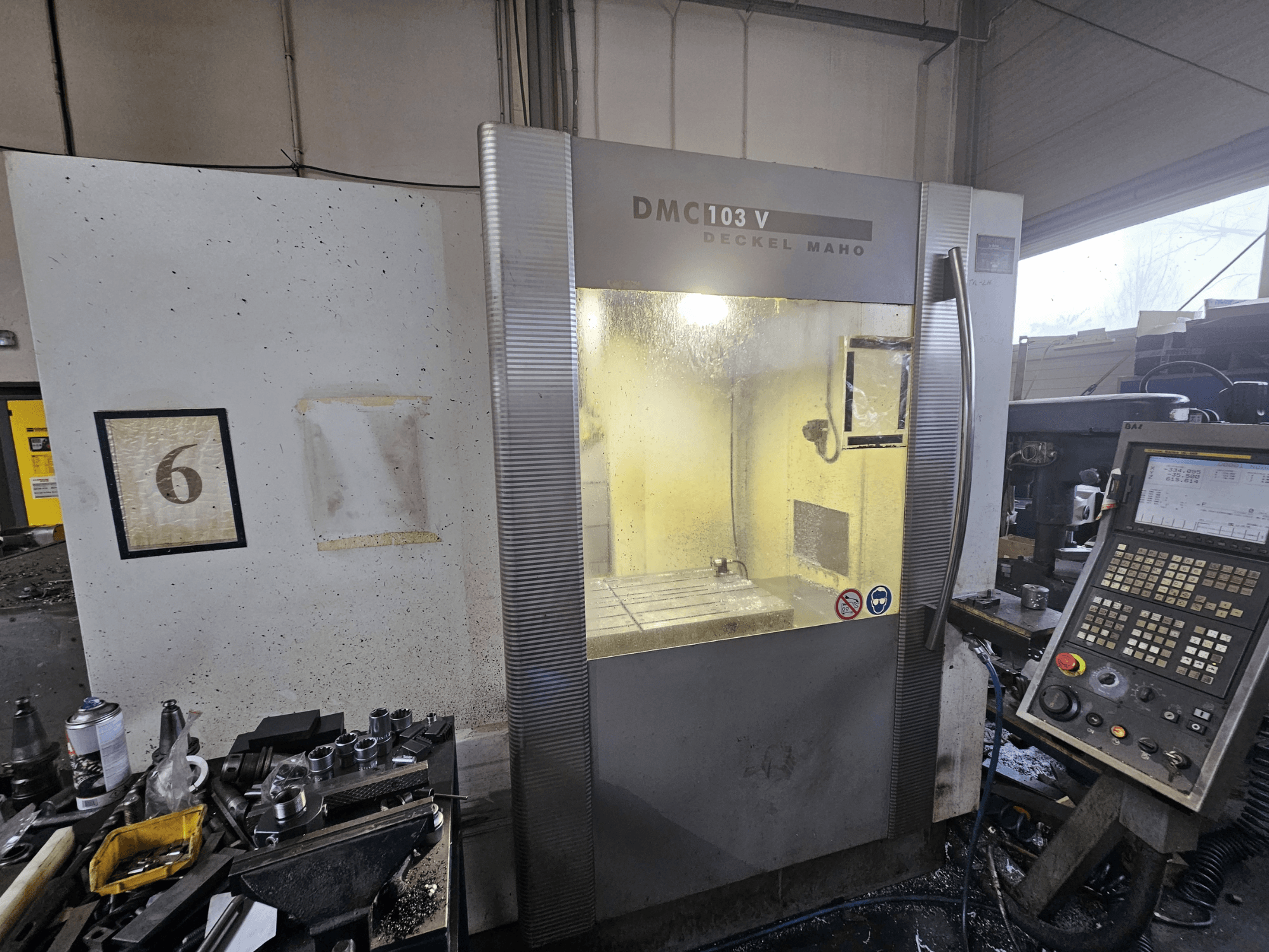 Macchina CNC Deckel Maho DMC 103 V, vista frontale, con pannello di controllo e area di lavoro, con il numero "6" sulla parete.