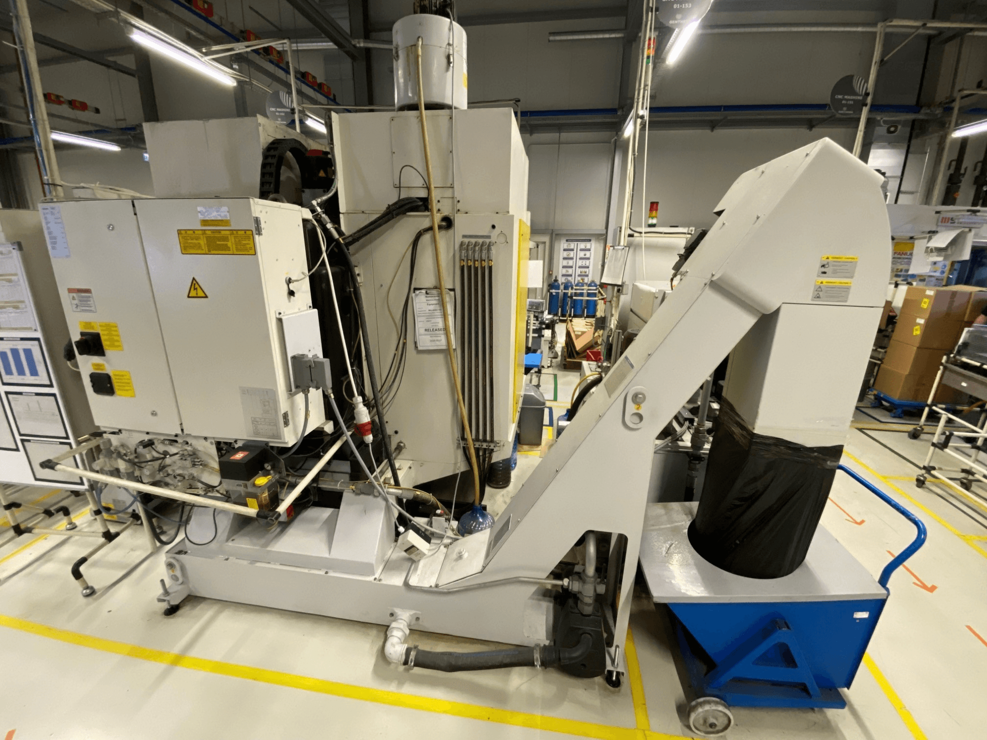 Vista frontale del centro di lavorazione verticale FANUC ROBODRILL α-D21LiB, con i componenti elettrici e lo scivolo di scarico in primo piano.