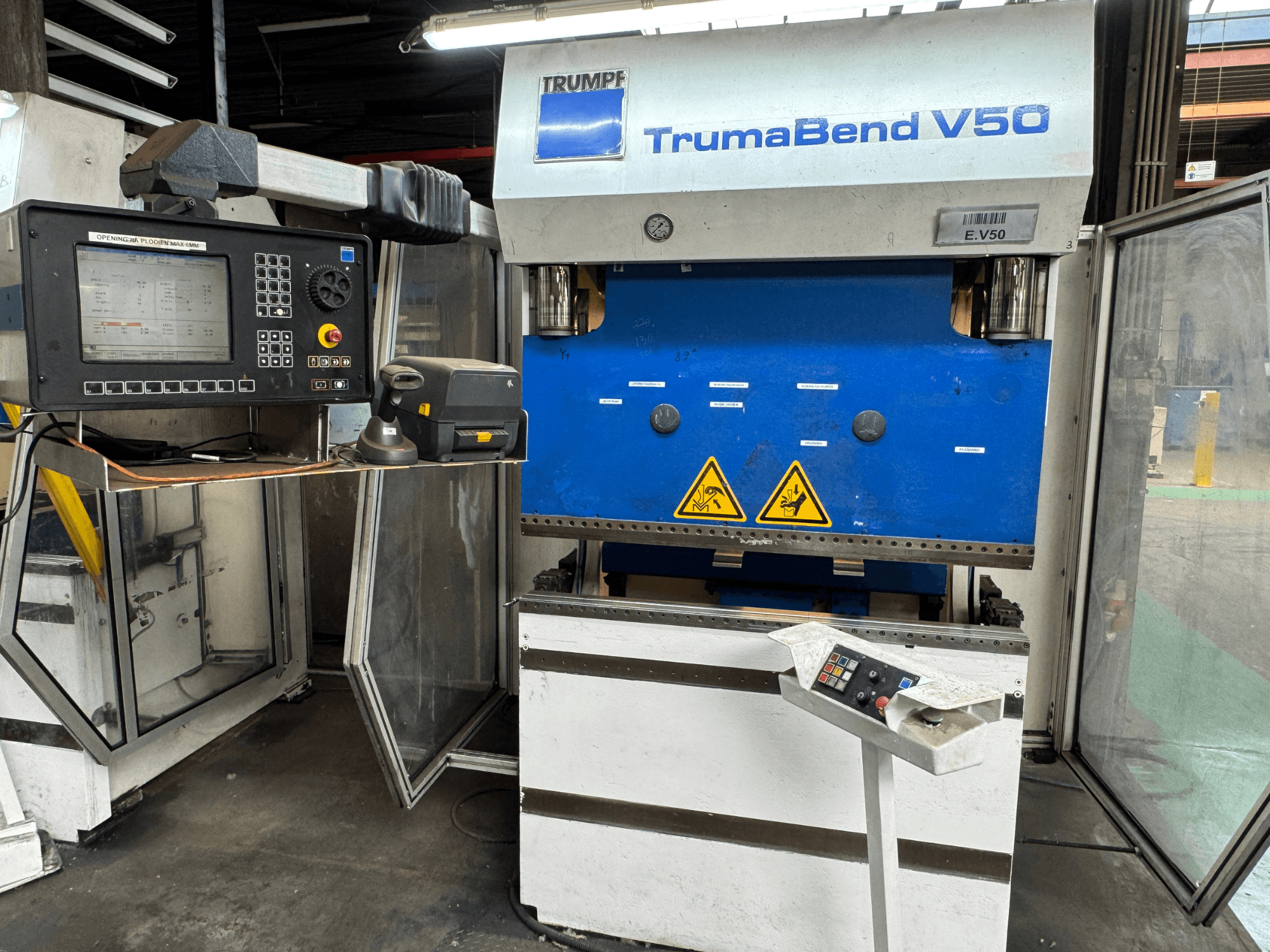 La pressa piegatrice TRUMPF TrumaBend V50 vista frontalmente, con il pannello di controllo, le avvertenze di sicurezza e il caratteristico design blu e bianco.