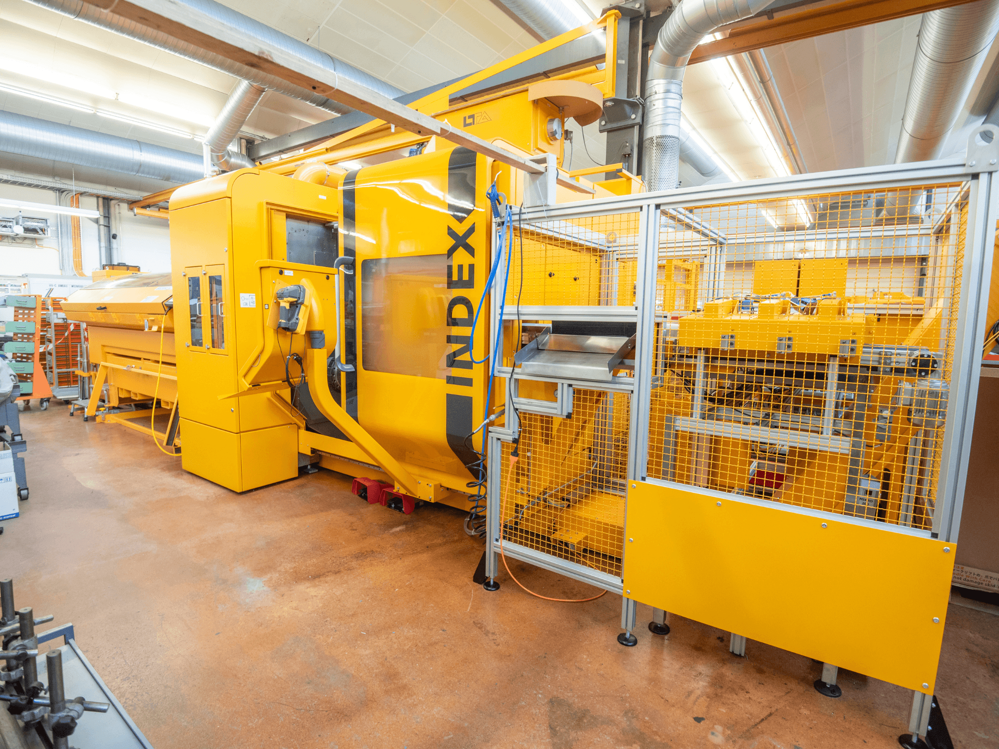 Macchina INDEX gialla in un'officina, vista frontale. Presenta un involucro di sicurezza, un pannello di controllo e diversi componenti operativi.
