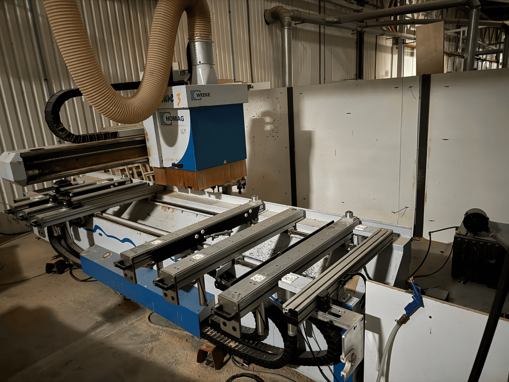 Macchina CNC HOMAG con design blu e bianco, vista laterale, dotata di guide scorrevoli, sistema di aspirazione della polvere e utensili montati.