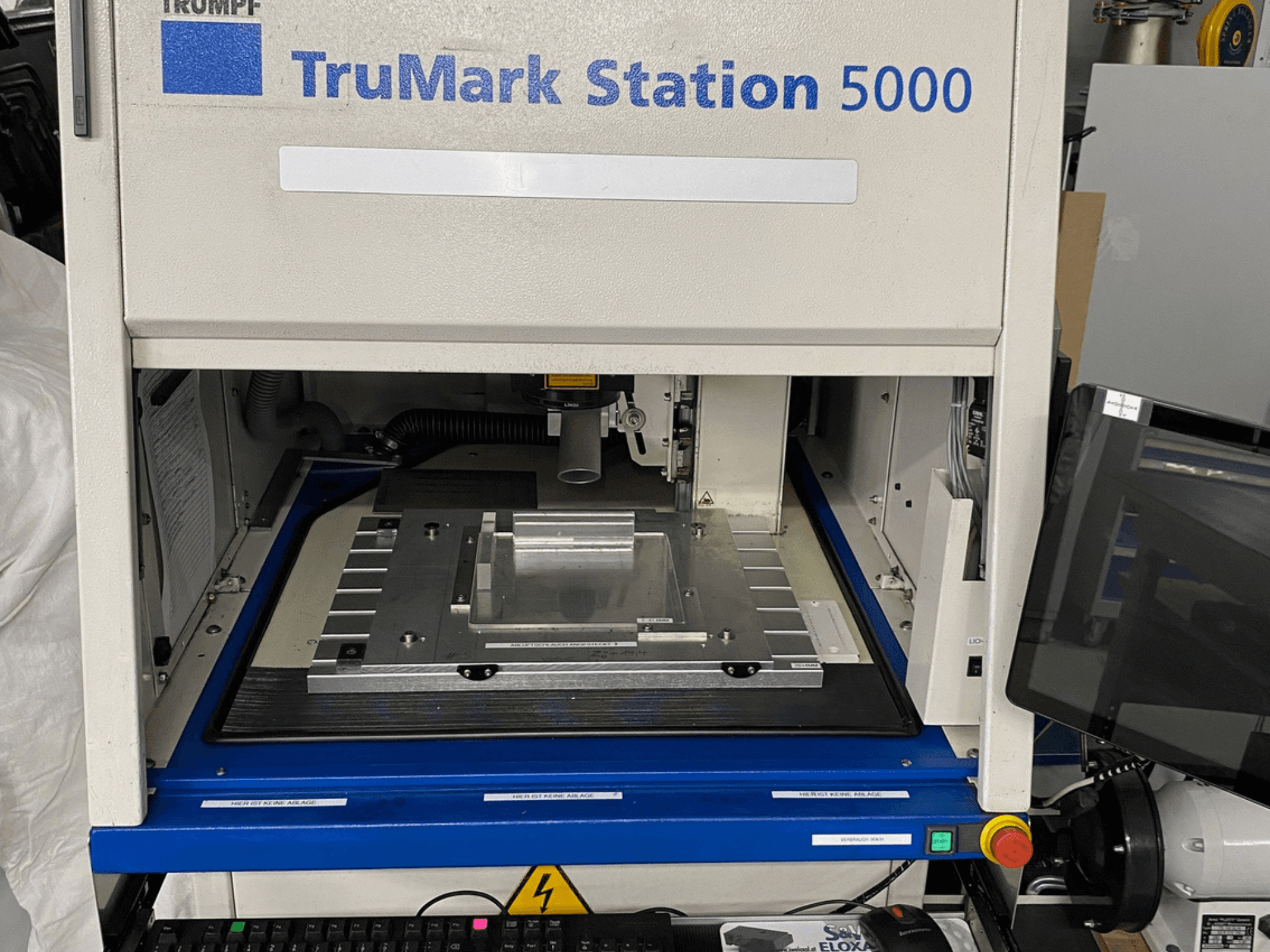 Vista frontale della macchina di marcatura laser TruMark Station 5000 che mostra il tavolo di lavoro, i comandi e lo schermo di monitoraggio.