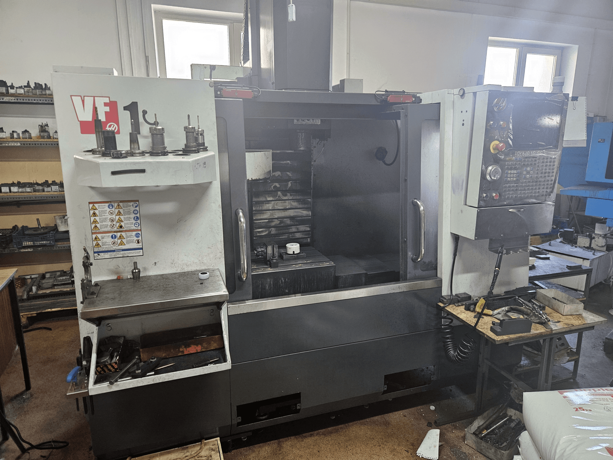 Centro di lavoro verticale HAAS VF-1, vista frontale con utensili sul lato, pannello di controllo visibile e area di lavoro sullo sfondo.