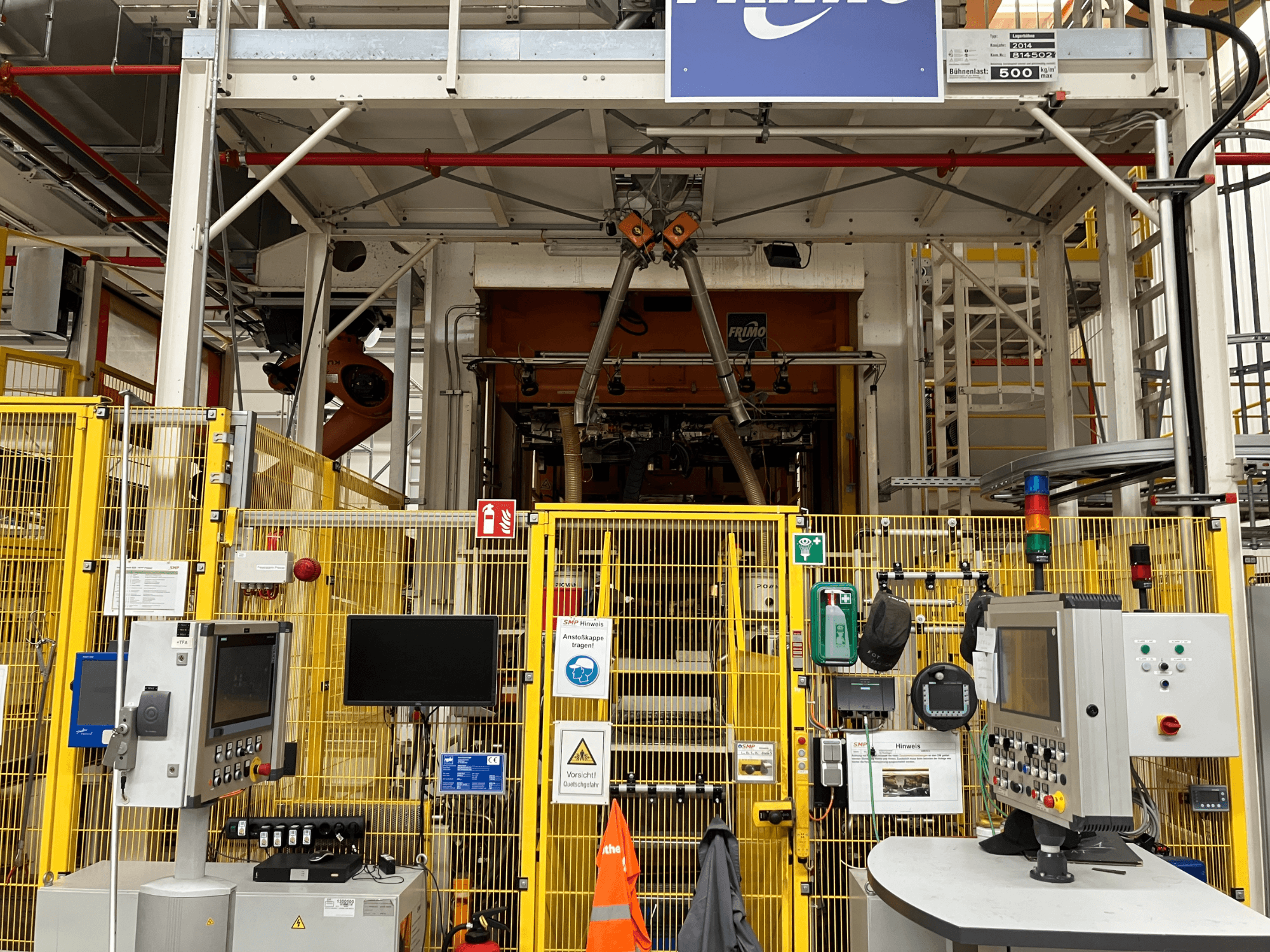 Vista frontale della centrale di termoformatura FRIMO NFPP, con pannelli di controllo e recinzioni di sicurezza in un ambiente industriale ben illuminato.
