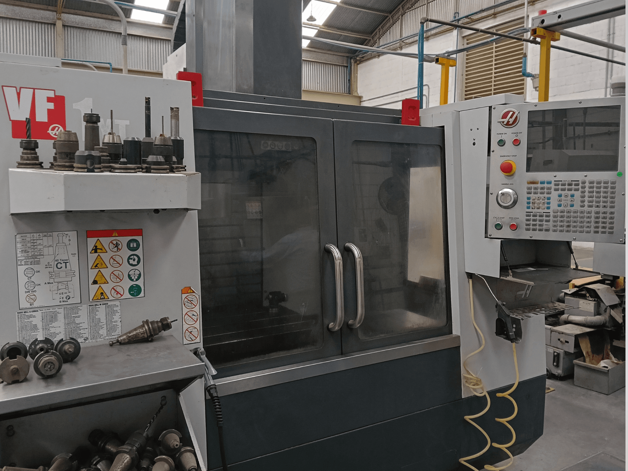 Centro di lavorazione verticale HAAS VF-1YT-3 visto frontalmente, con in primo piano i comandi, i portautensili e le etichette di sicurezza ben visibili.