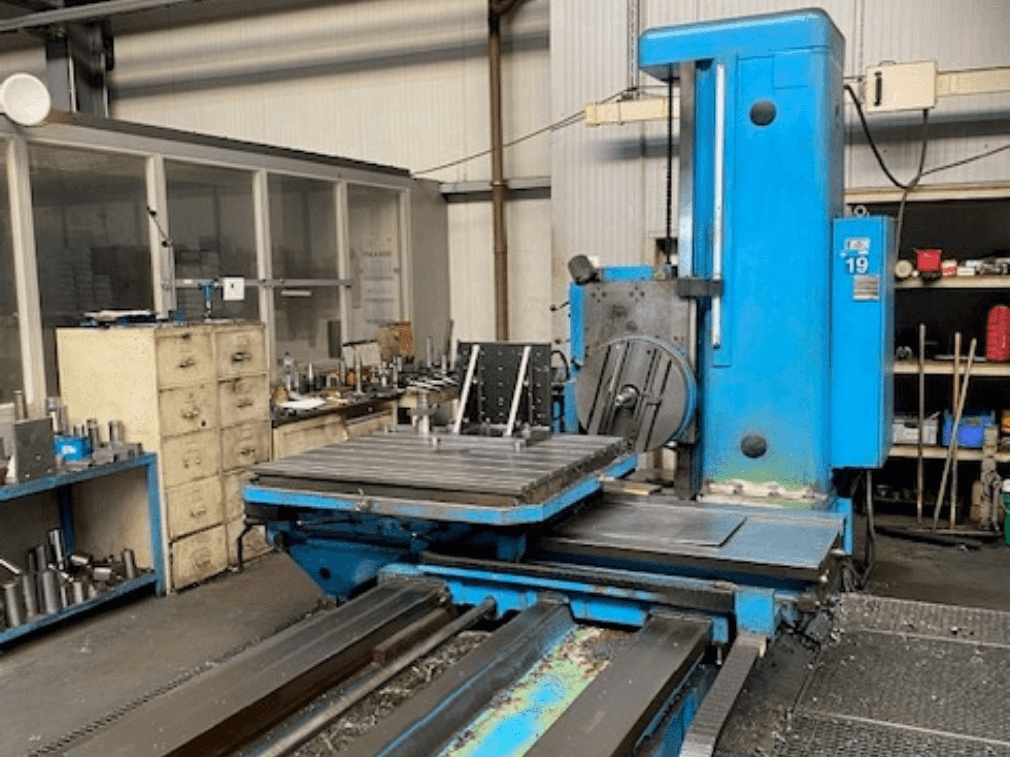 Fresatrice blu in vista frontale, modello numero 19, sul pavimento di un'officina con attrezzi e un armadio di stoccaggio sullo sfondo.