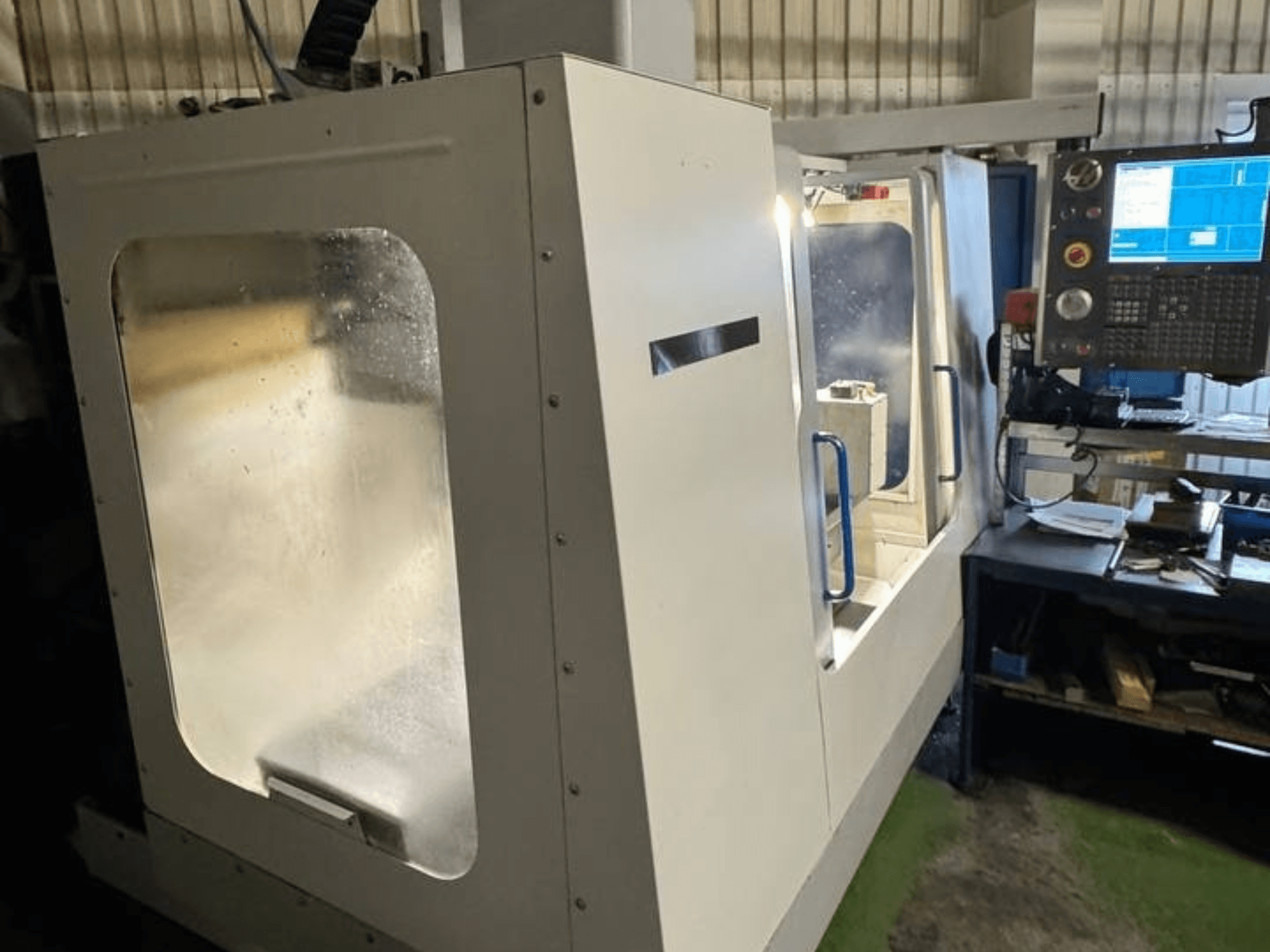 Centro di lavoro verticale HAAS VCE 750 in vista laterale, caratterizzato da un pannello di controllo e da un involucro di sicurezza trasparente.